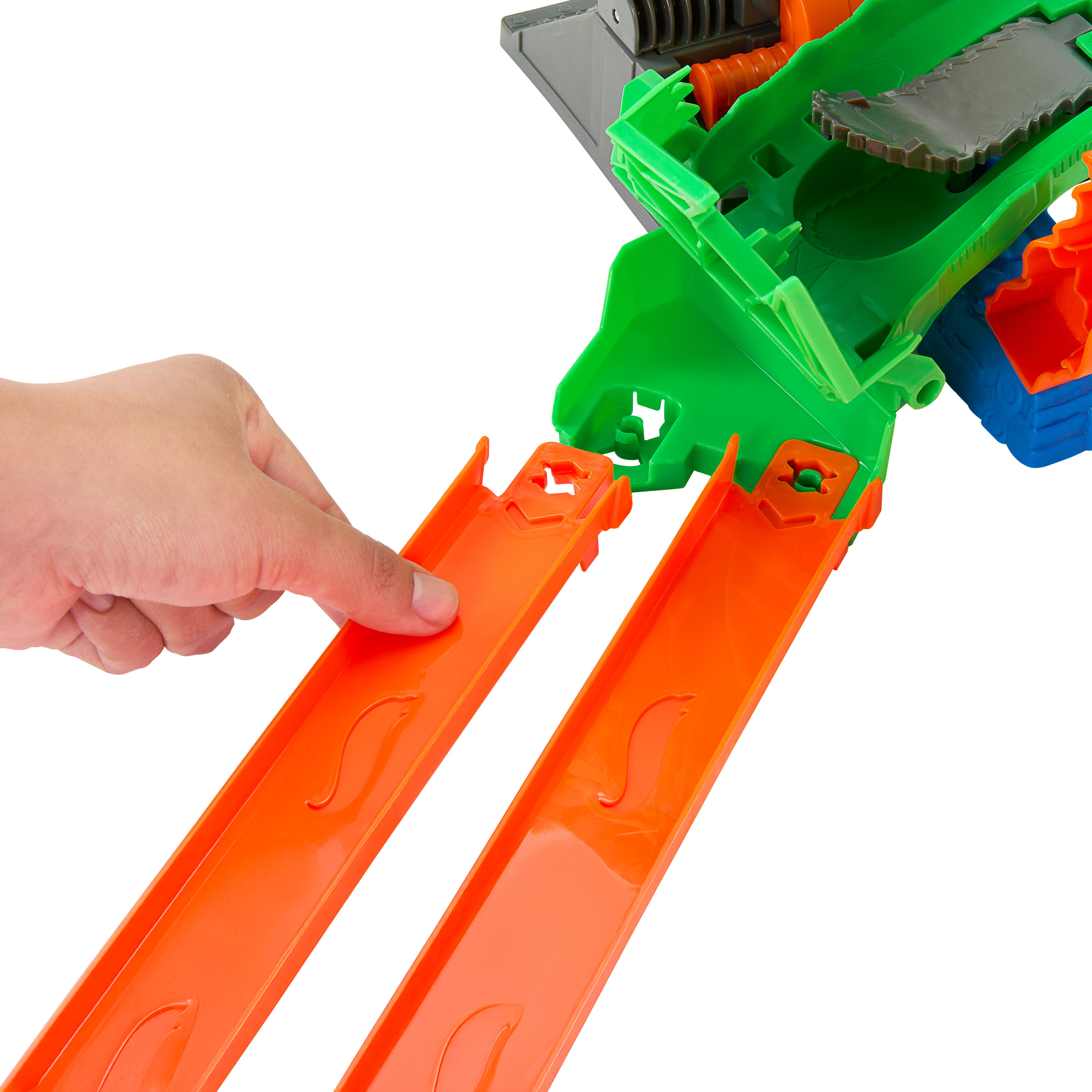 Dłoń dotyka pomarańczowego toru. Zielone i szare plastikowe elementy zabawki znajdują się za torami.