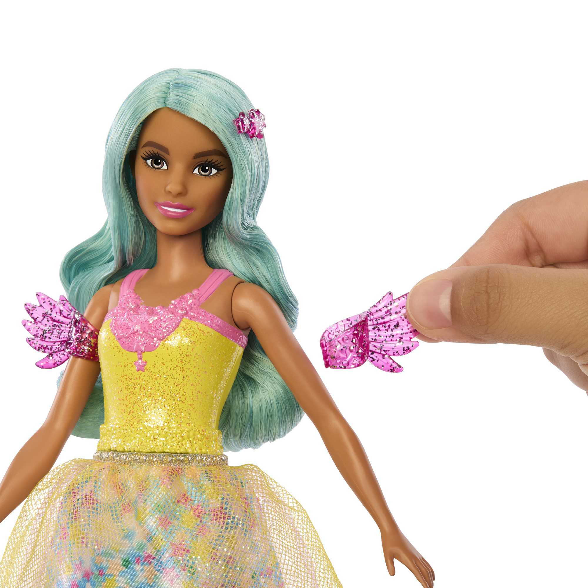 Lalka z turkusowymi włosami i żółtą sukienką. Ręka trzyma różowy dodatek ze skrzydłem.