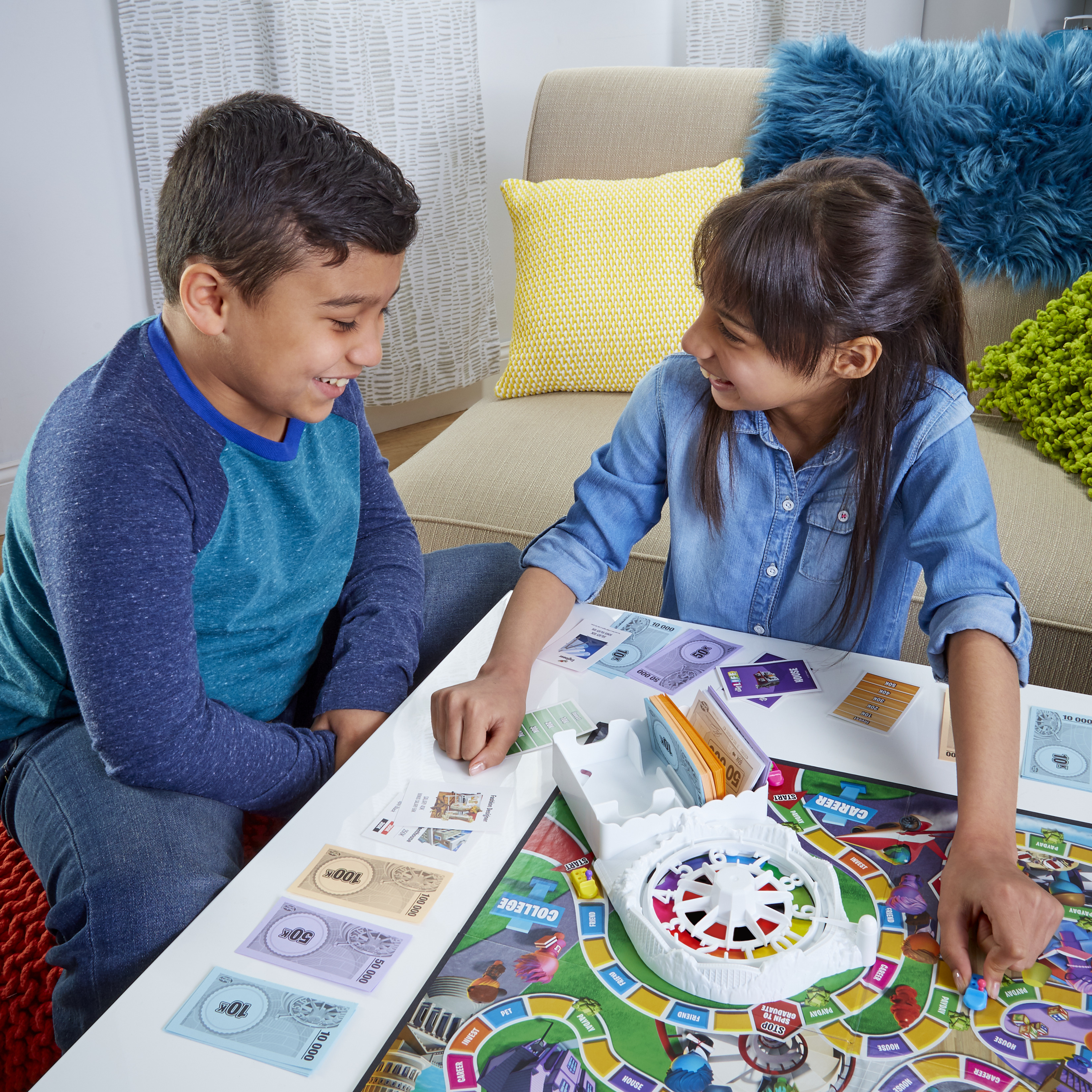 Twee kinderen spelen een bordspel, glimlachend. Het spelbord is zichtbaar, samen met geld en pionnen.