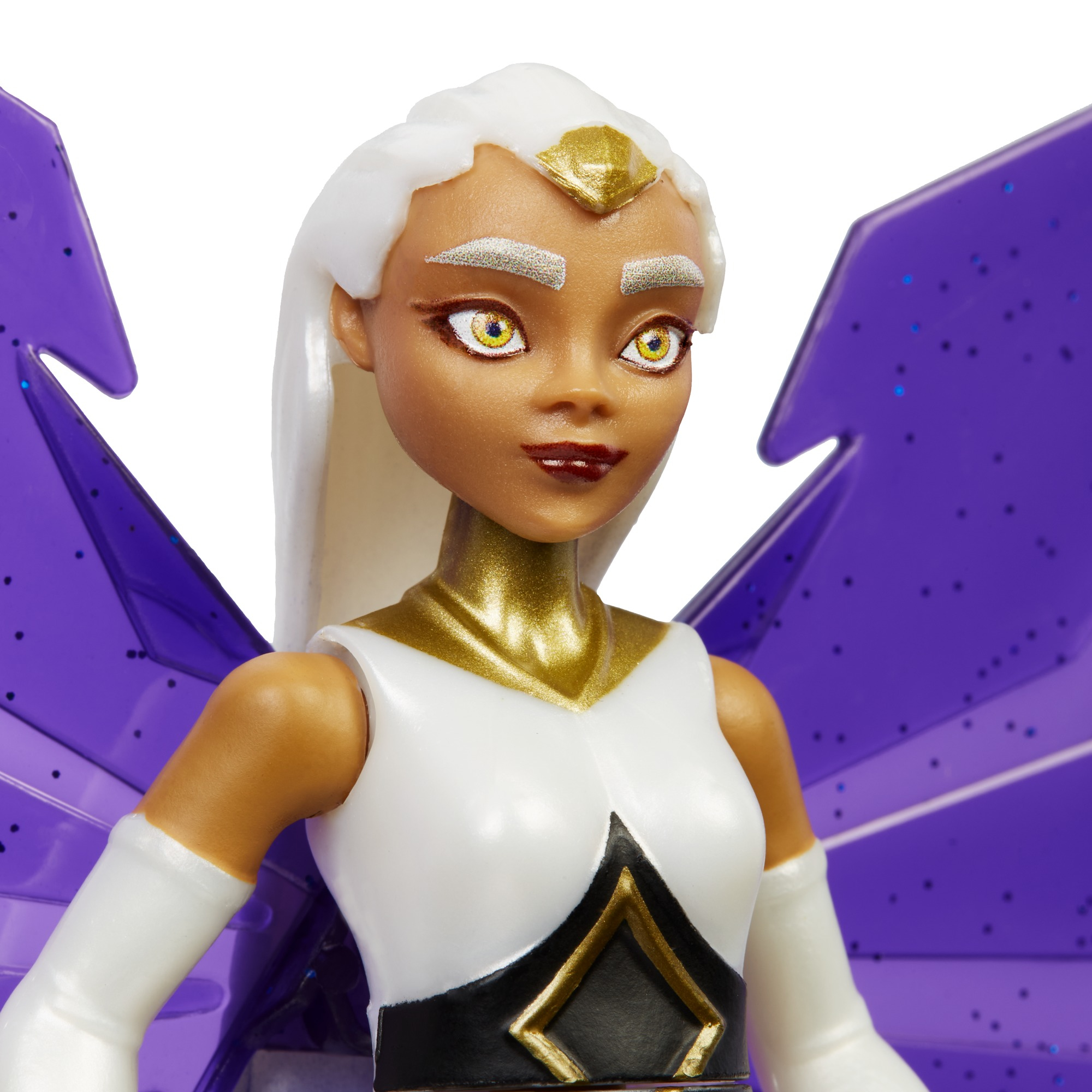 Una muñeca con pelo blanco, alas moradas, detalles dorados y un atuendo blanco y negro. La muñeca mira hacia un lado.