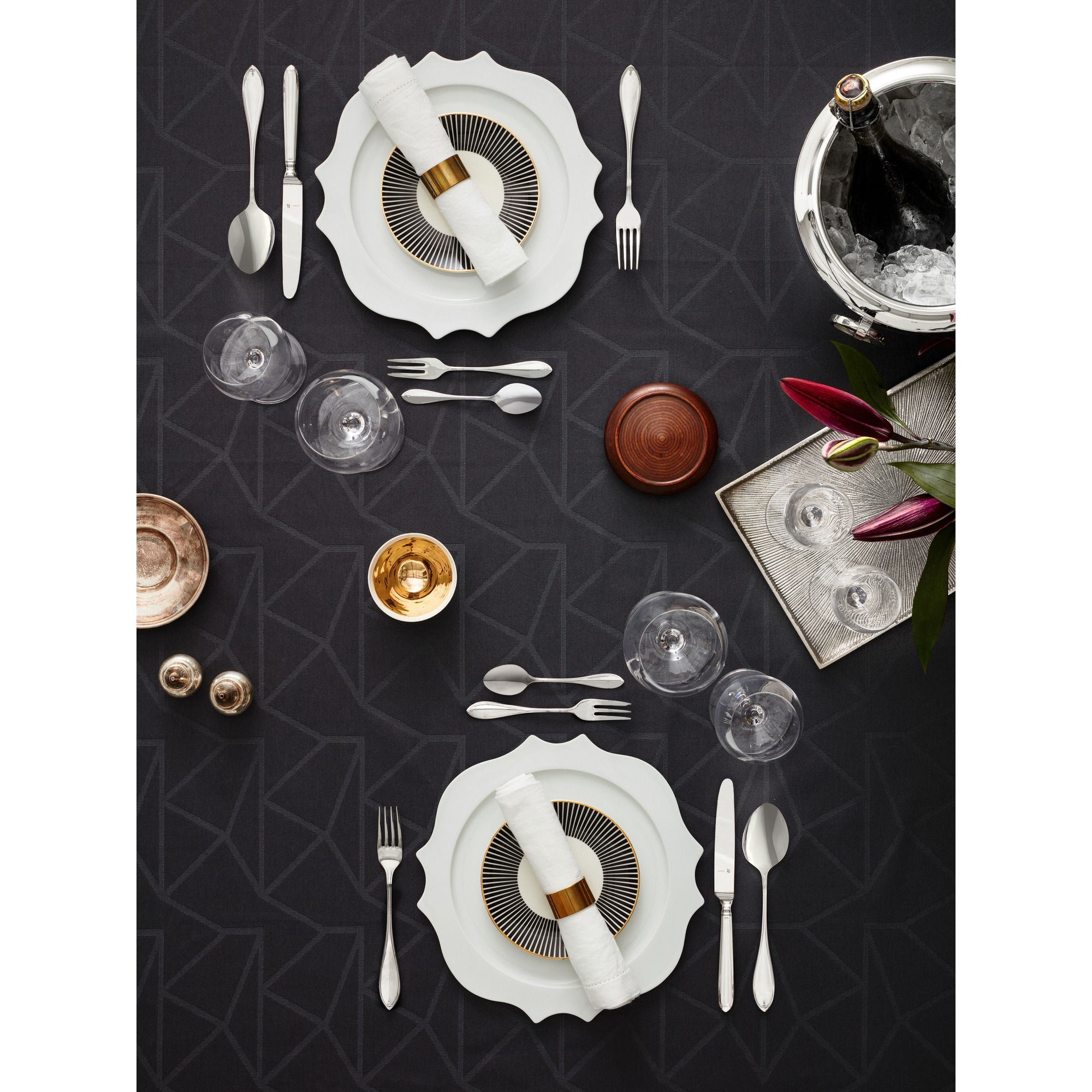 Formele dineropstelling. Borden met servetten, bestek, glazen, een champagne-emmer en bloemen zijn gerangschikt op een zwart patroon.