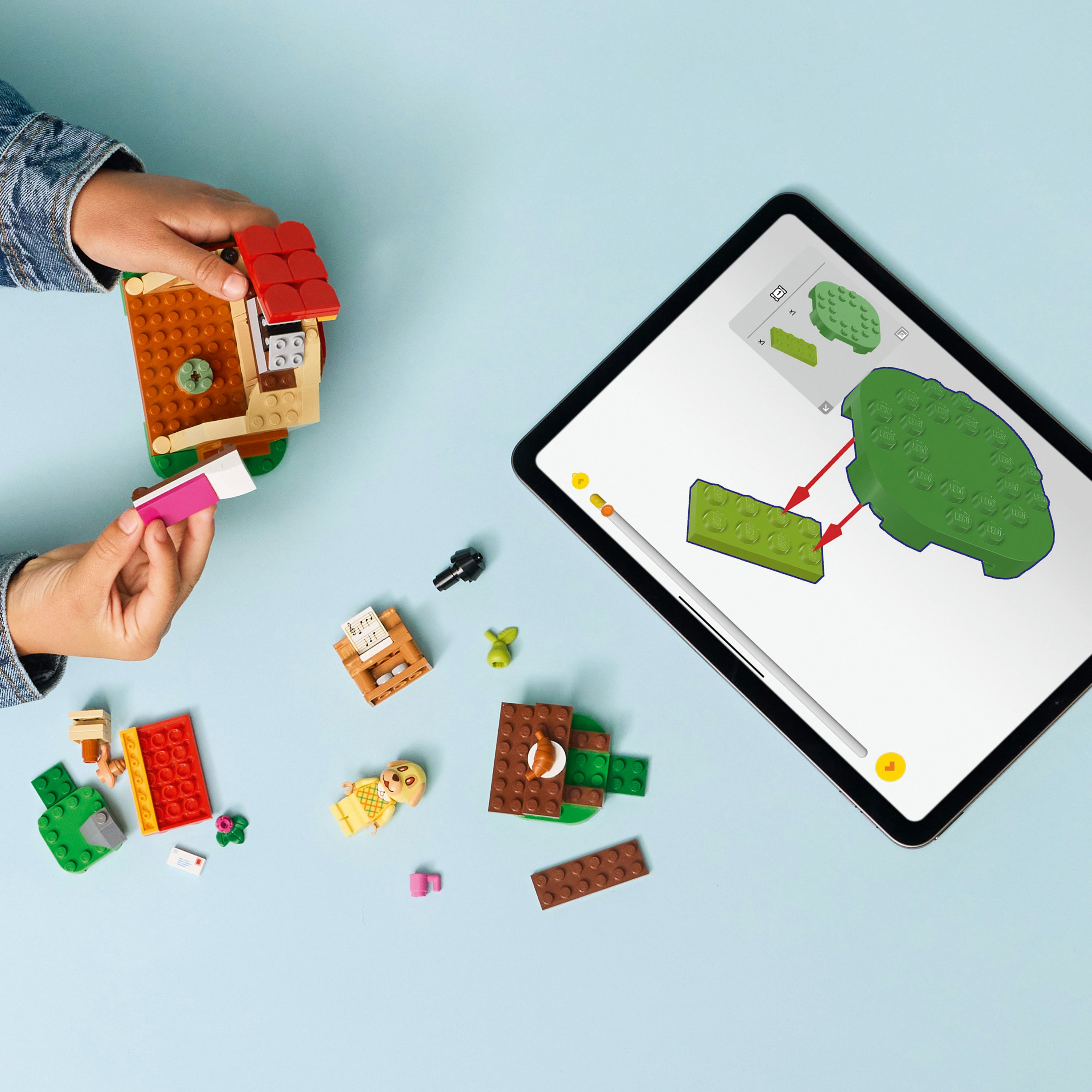 Dziecko buduje domek z Lego obok tabletu z instrukcjami. Różne klocki Lego są rozrzucone.