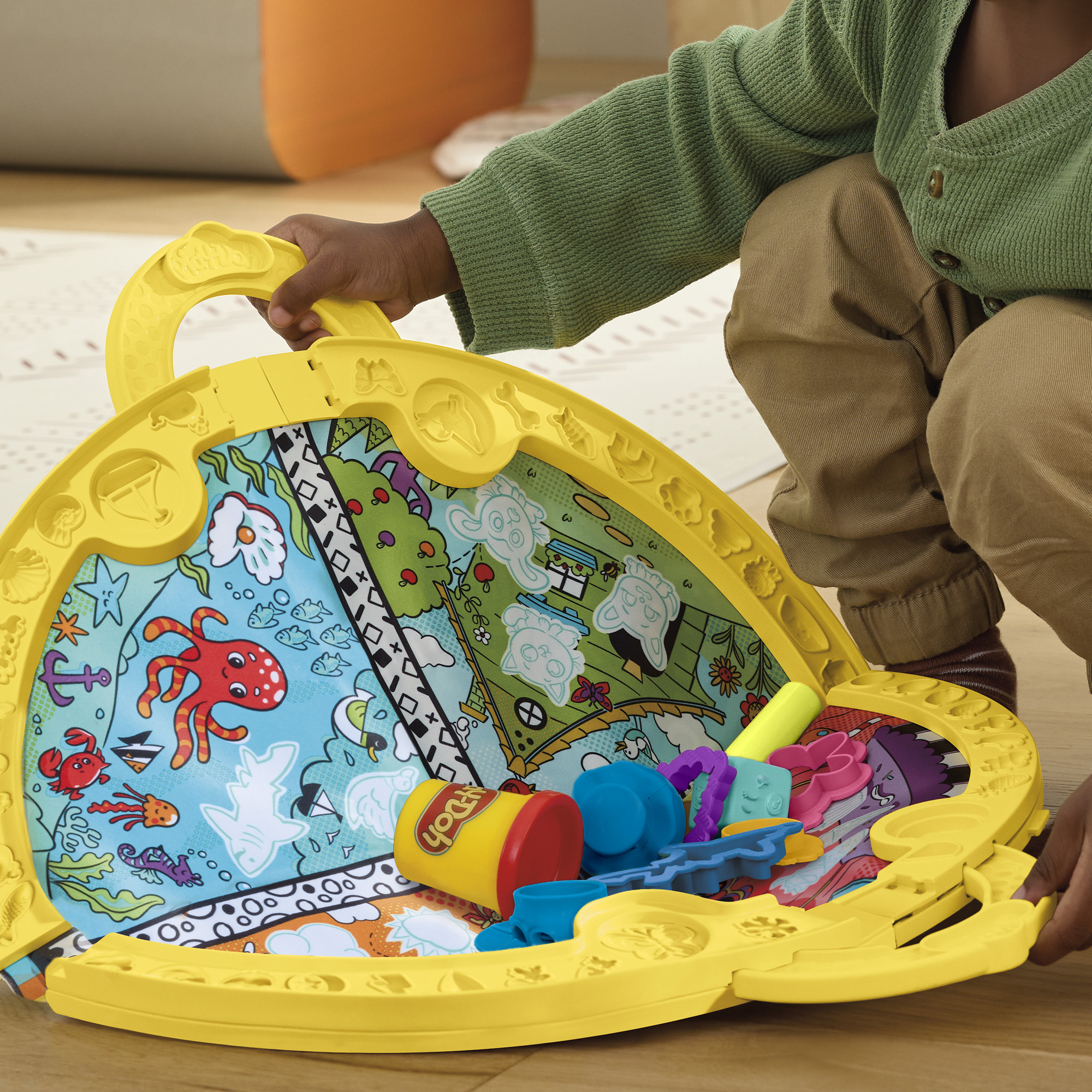 Un niño juega con un juego Play-Doh amarillo. Tiene criaturas marinas dibujadas en el interior y herramientas Play-Doh.