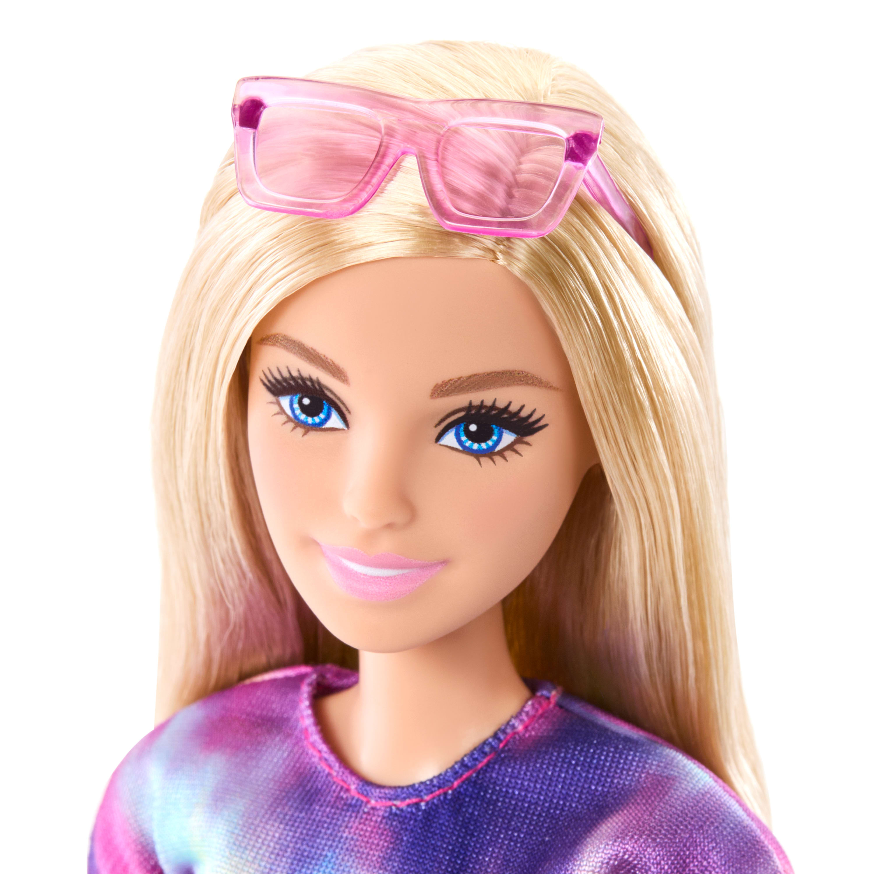 Eine Barbie-Puppe mit blondem Haar, blauen Augen und einer rosa Sonnenbrille. Sie trägt ein Batik-Shirt und lächelt.