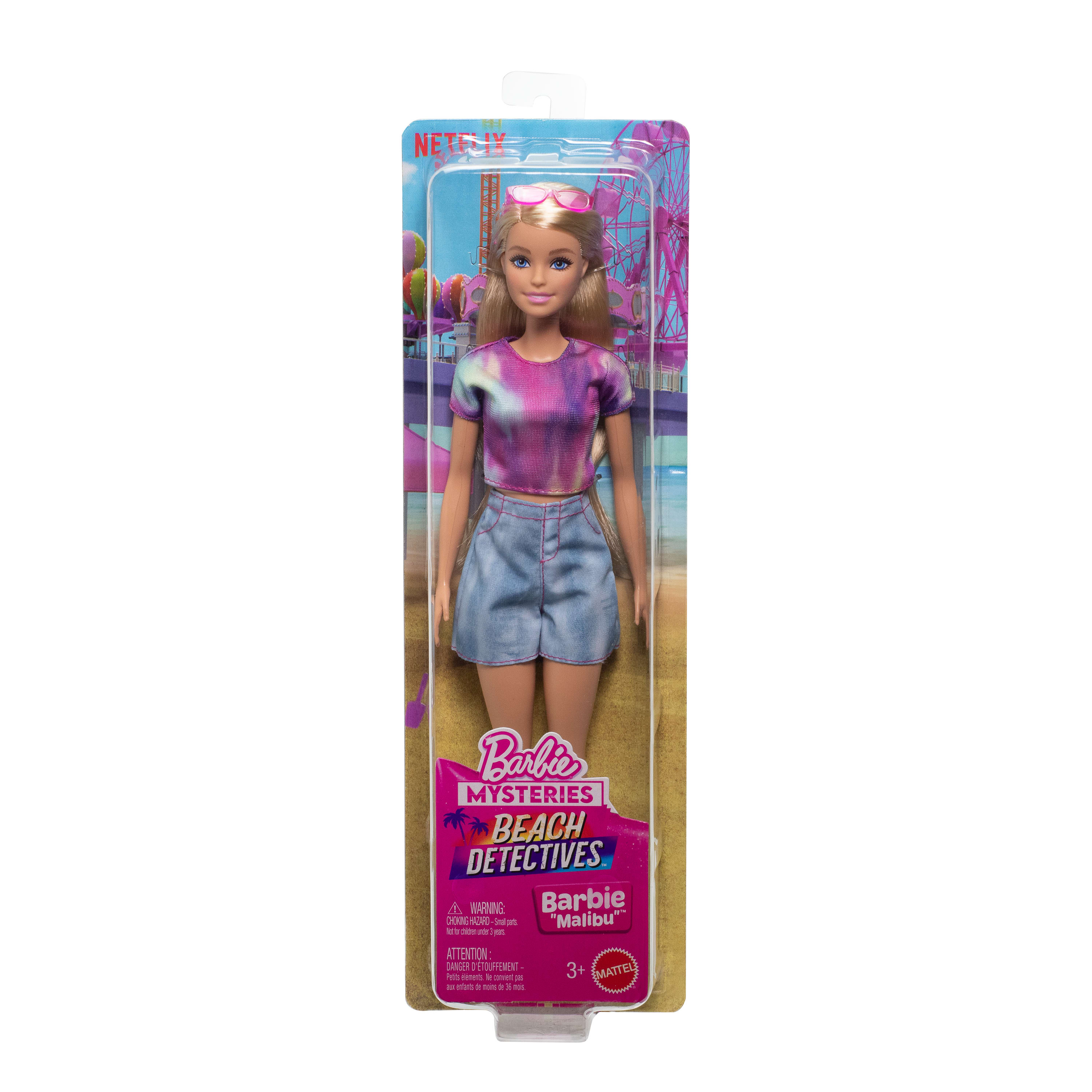Barbie-Puppe in Verpackung. Sie trägt ein Batik-Shirt, Jeansshorts und eine Sonnenbrille. Auf der Verpackung steht 'Beach Detectives'.