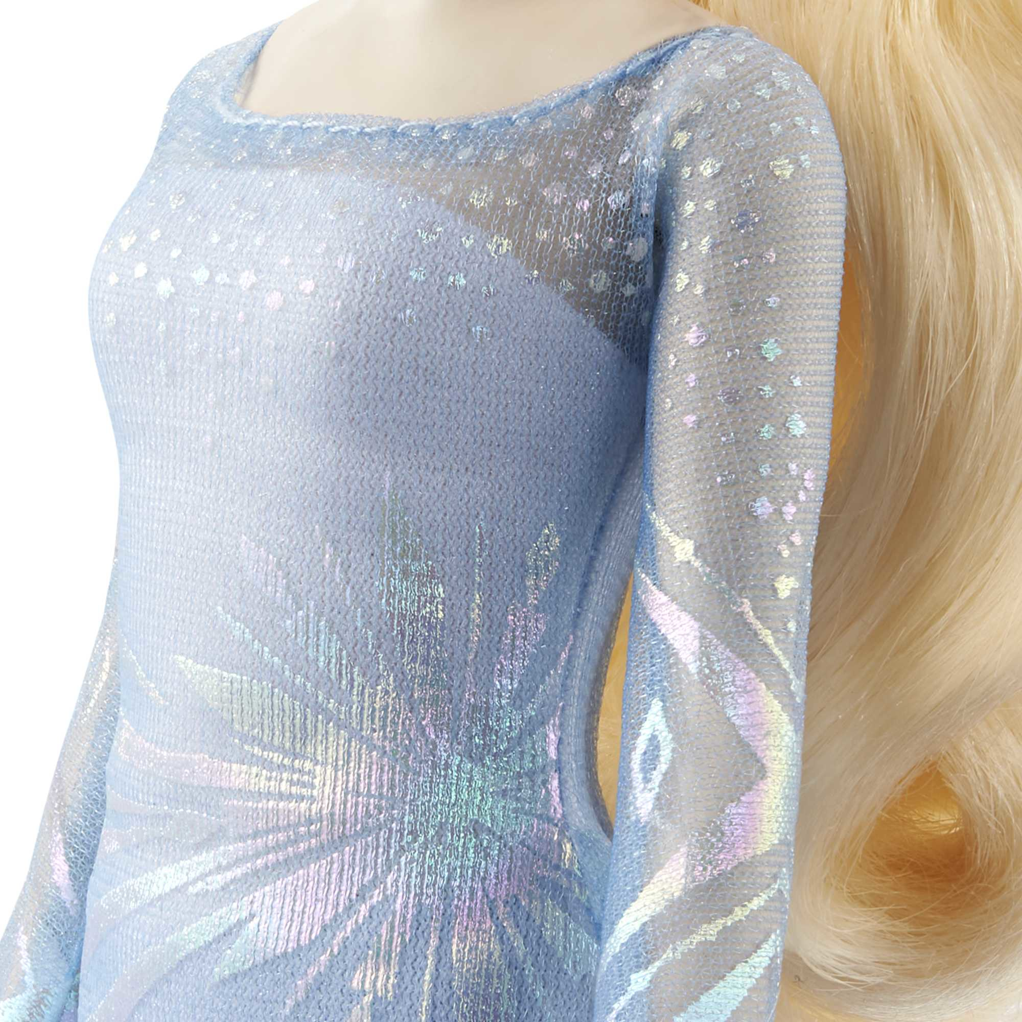 Eine Puppe in einem hellblauen Kleid mit komplizierten Mustern und blonden Haaren. Das Kleid hat einen durchsichtigen Überzug mit glitzernden Details.