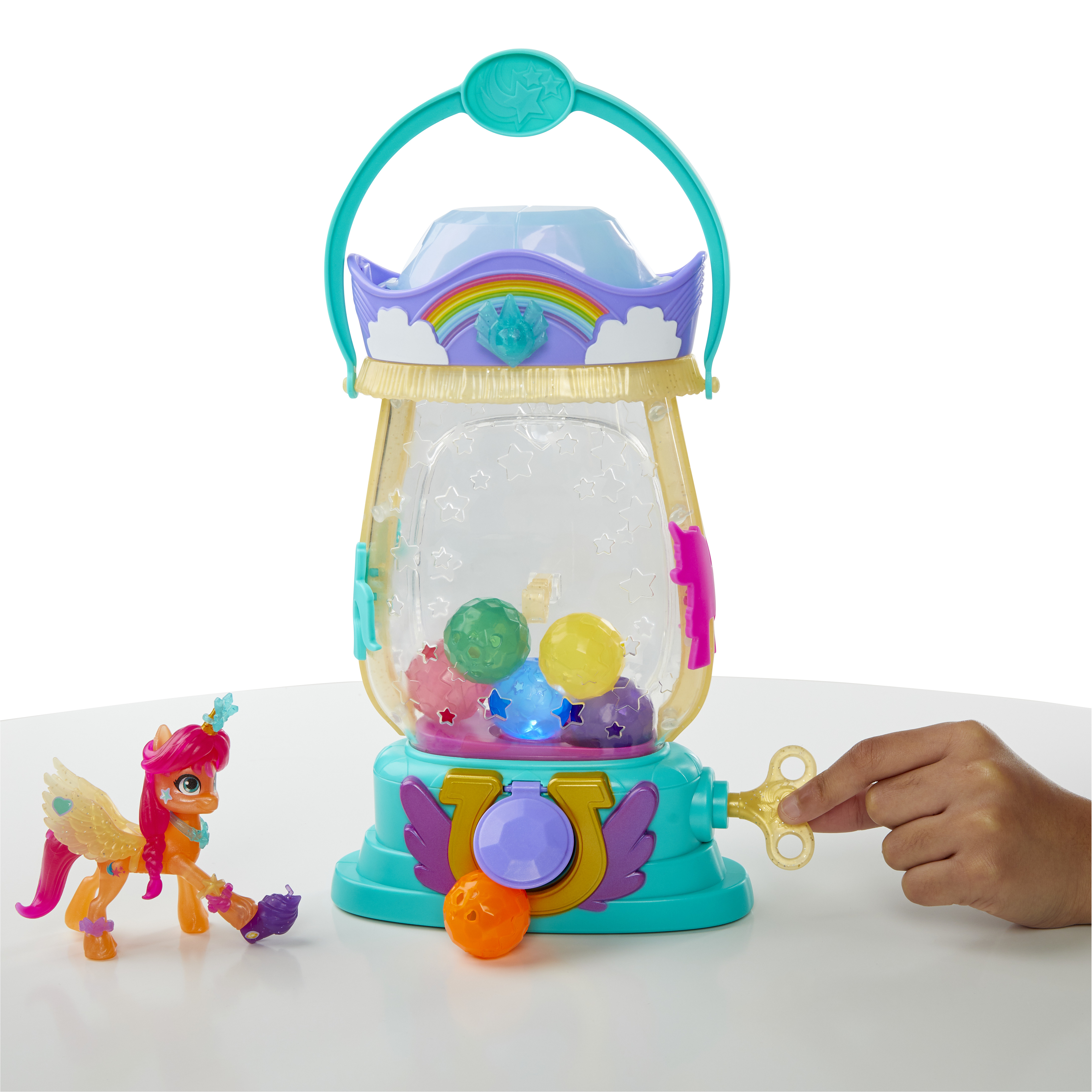 Un juguete con una figura de pony y una estructura similar a una máquina de chicles. Una mano gira una llave en el juguete.
