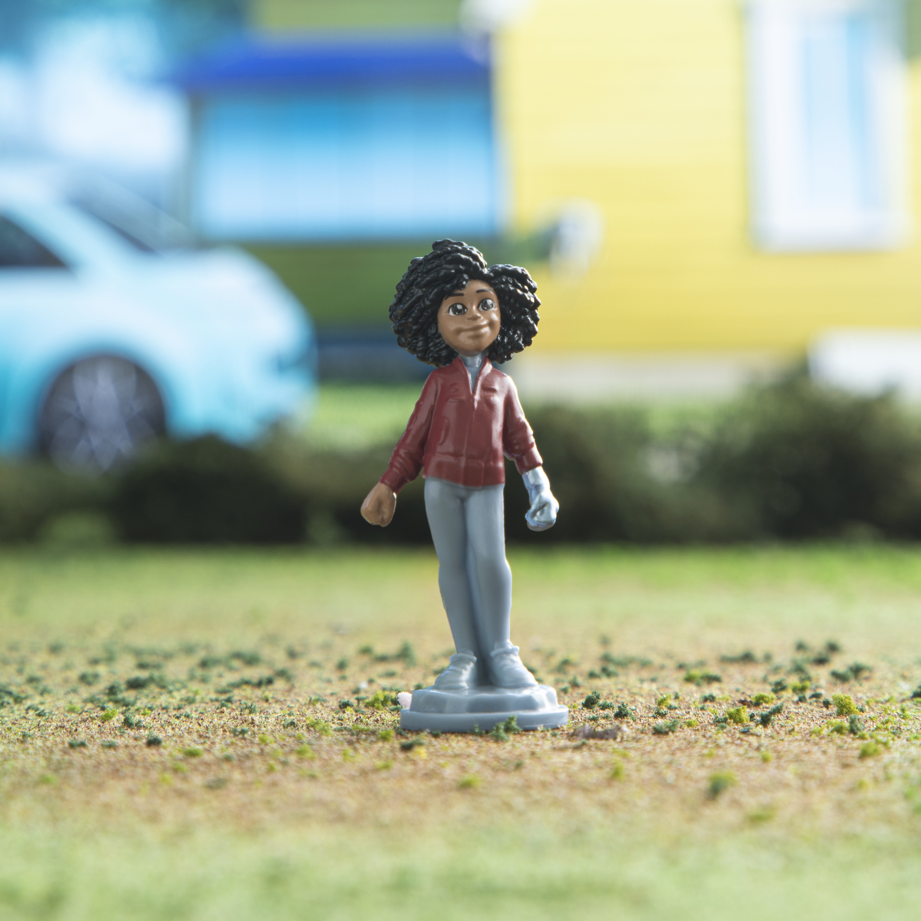 Una figura de una persona frente a una casa. La figura lleva una camisa roja y pantalones grises.