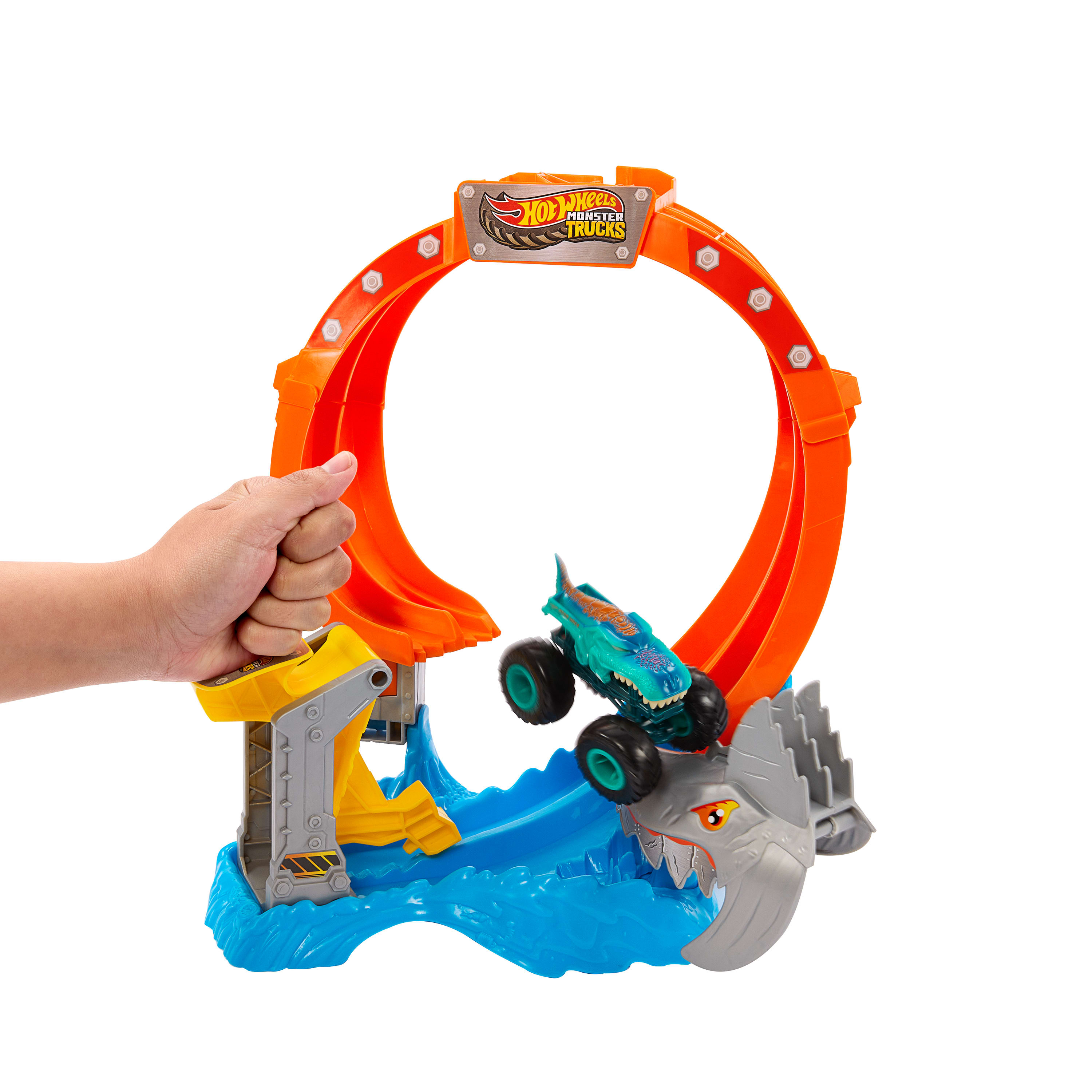 Eine Hand hält ein Hot Wheels Monster Trucks Spielset mit einer Schleife und einem springenden Monstertruck.