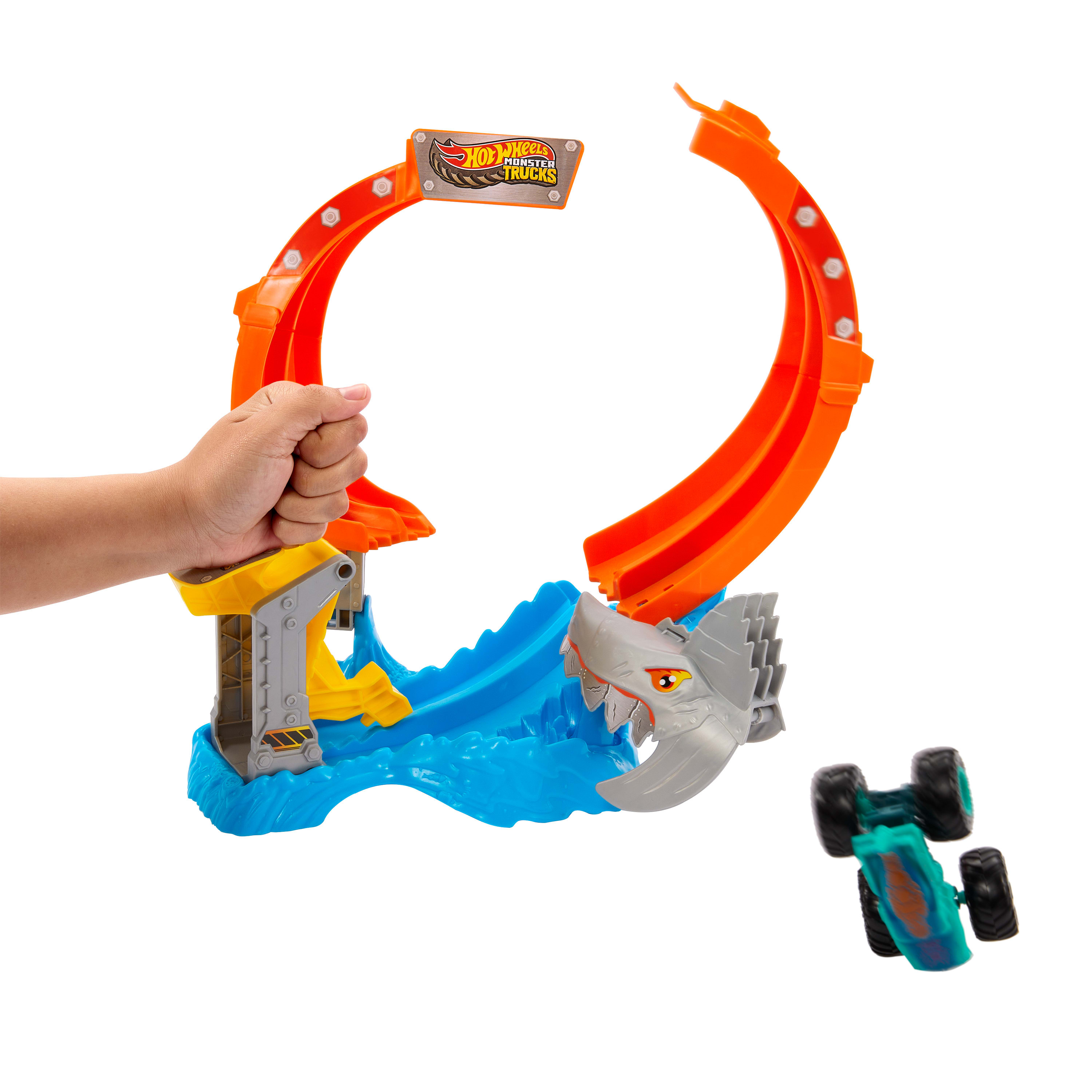 Die Hand eines Kindes hält eine orangefarbene Hot-Wheels-Strecke. Ein haiartiges Hindernis und ein Spielzeugauto sind vorhanden.