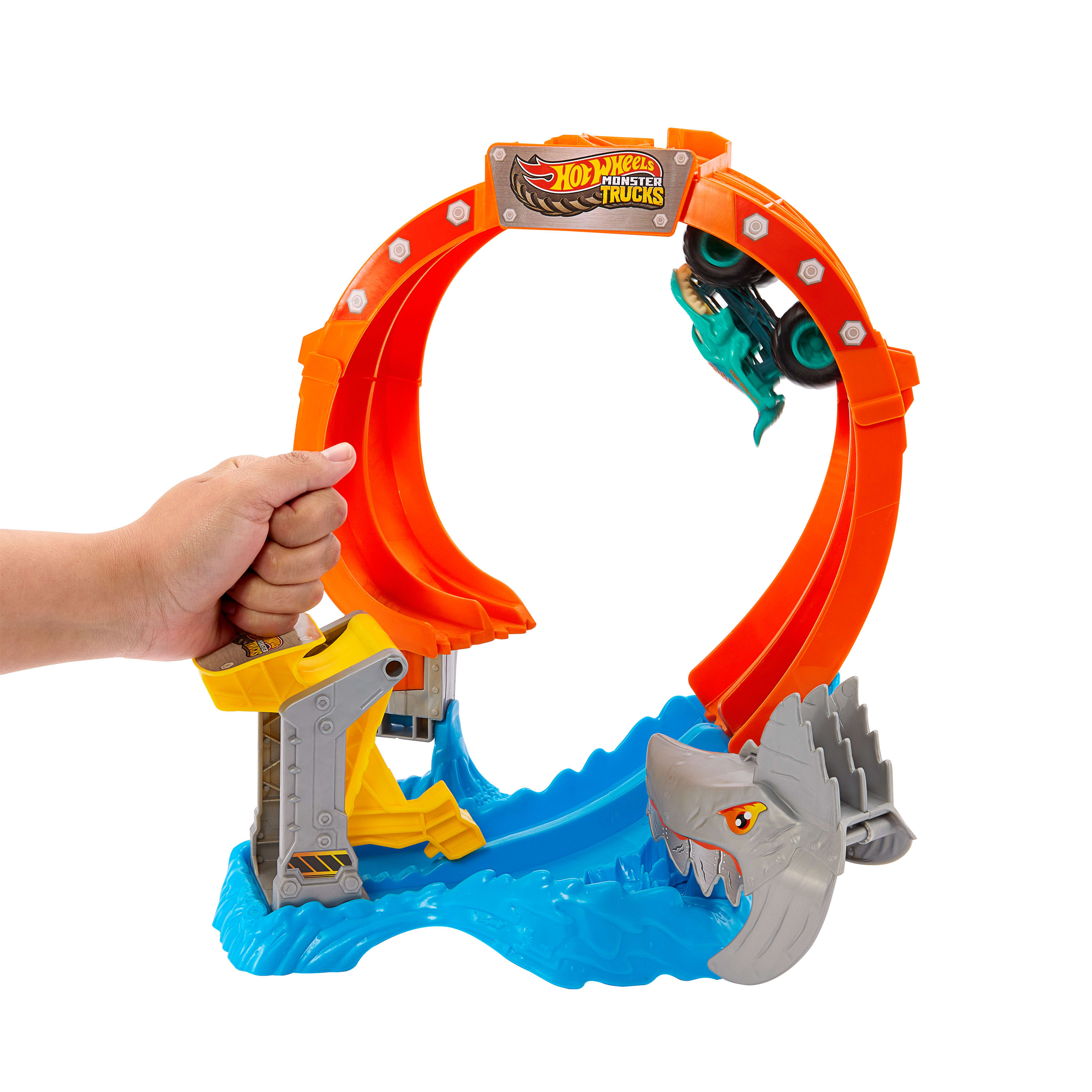 Eine Hand hält ein Hot Wheels Monster Trucks Spielset. Es zeigt eine Schleife, einen Hai und einen Monstertruck.