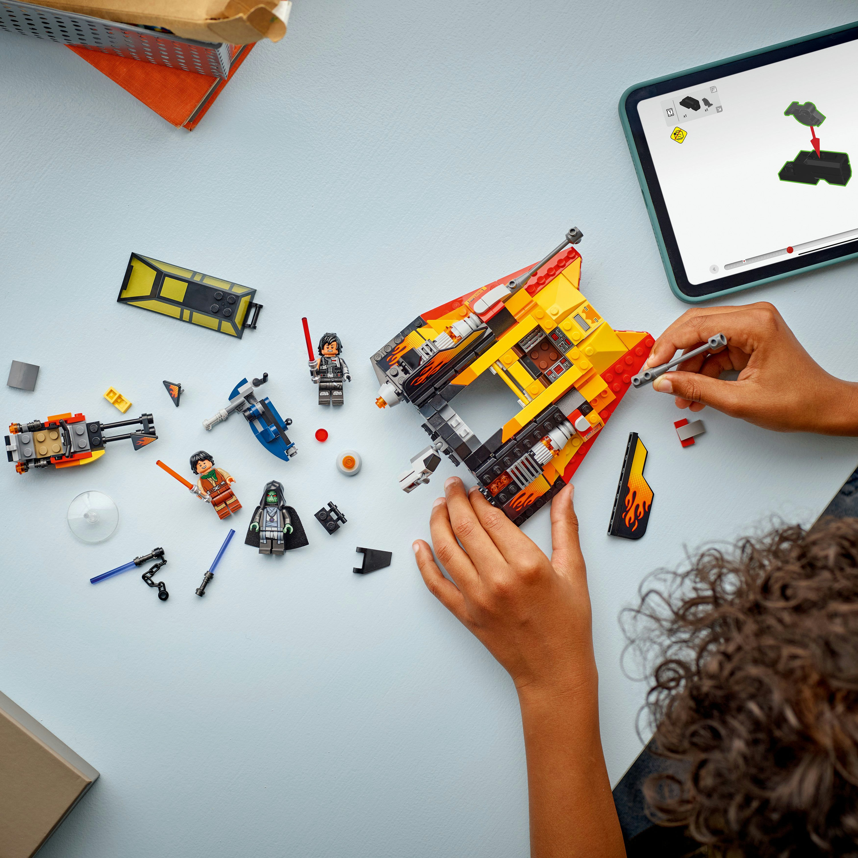 Osoba składająca statek Lego Star Wars. Części i minifigurki są rozrzucone na jasnoniebieskiej powierzchni. Tablet wyświetla instrukcje.