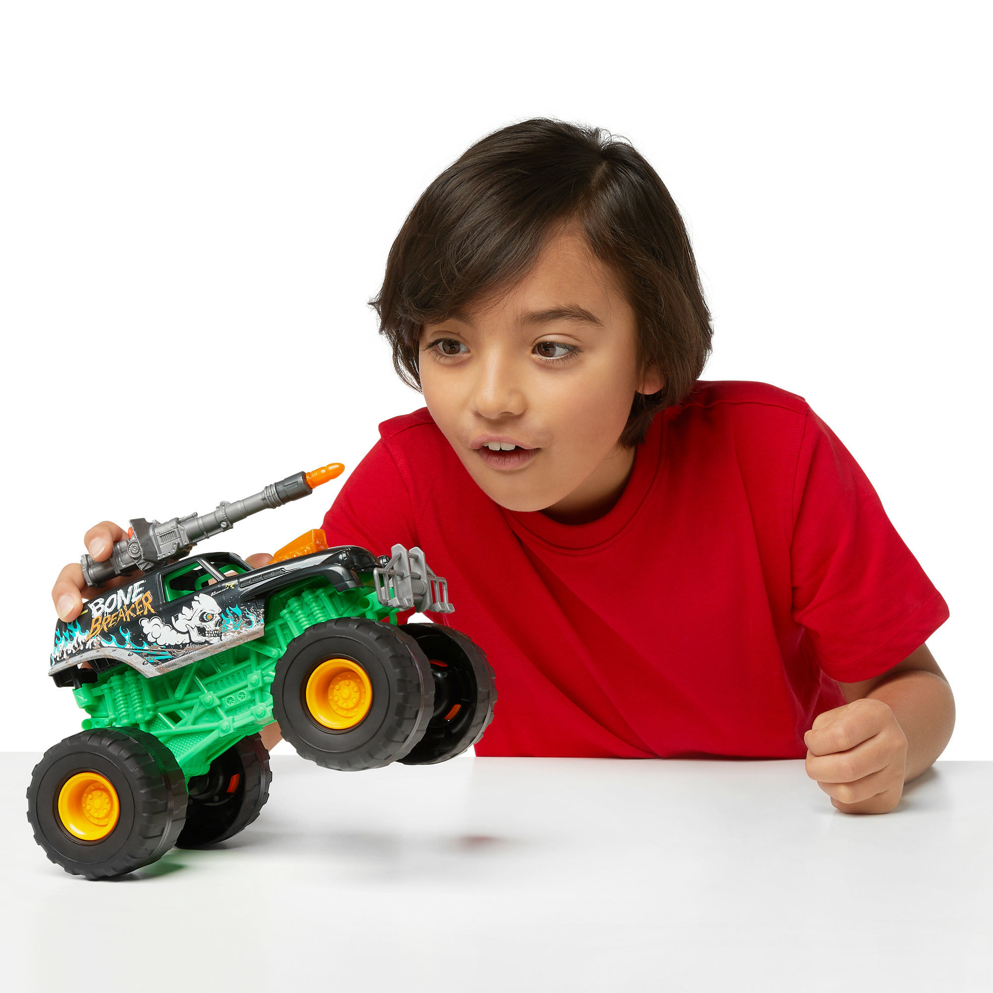 Chłopiec w czerwonej koszuli trzyma zieloną zabawkę monster truck z dołączoną bronią.