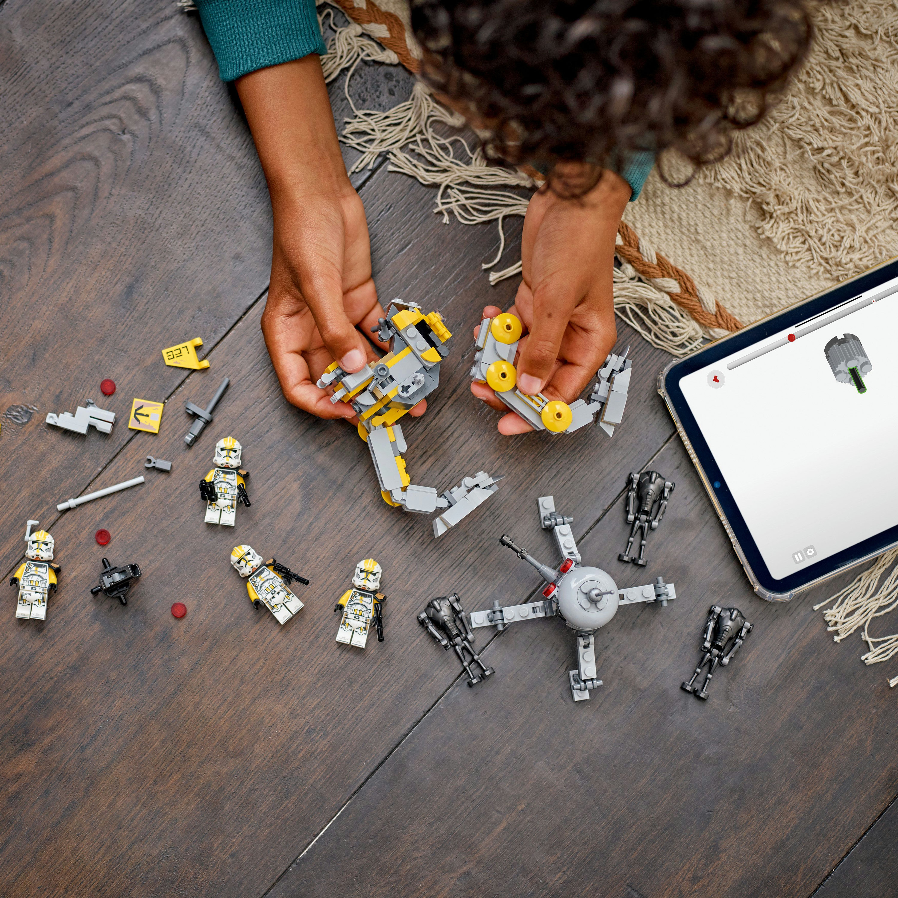 Ręce składają zestaw LEGO Star Wars na drewnianej powierzchni. Zawiera figurki, instrukcje na tablecie i inne elementy.