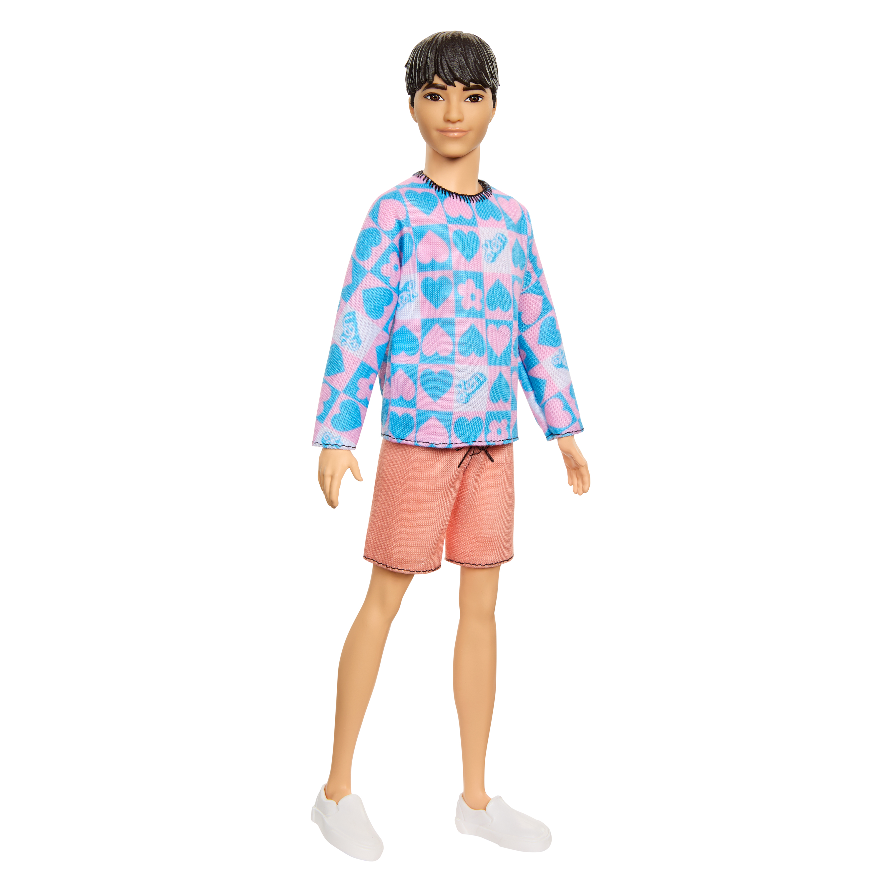 Eine Ken-Puppe steht da, trägt ein blau-rosa herzgemustertes Hemd, pfirsichfarbene Shorts und weiße Turnschuhe vor weißem Hintergrund.