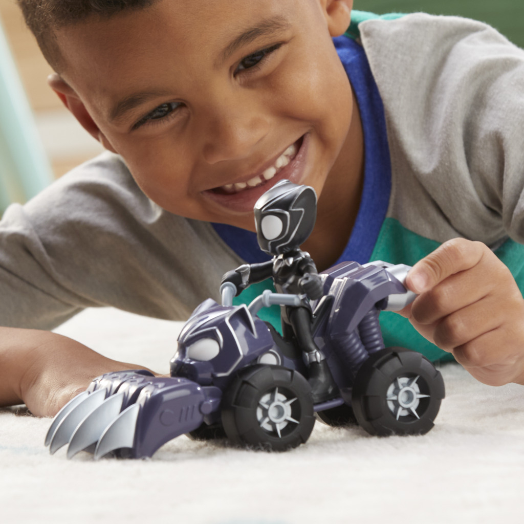 Uśmiechnięty chłopiec bawi się zabawką-samochodem i figurką akcji Black Panther. Samochód jest fioletowy i czarny. Chłopiec jest na pierwszym planie.