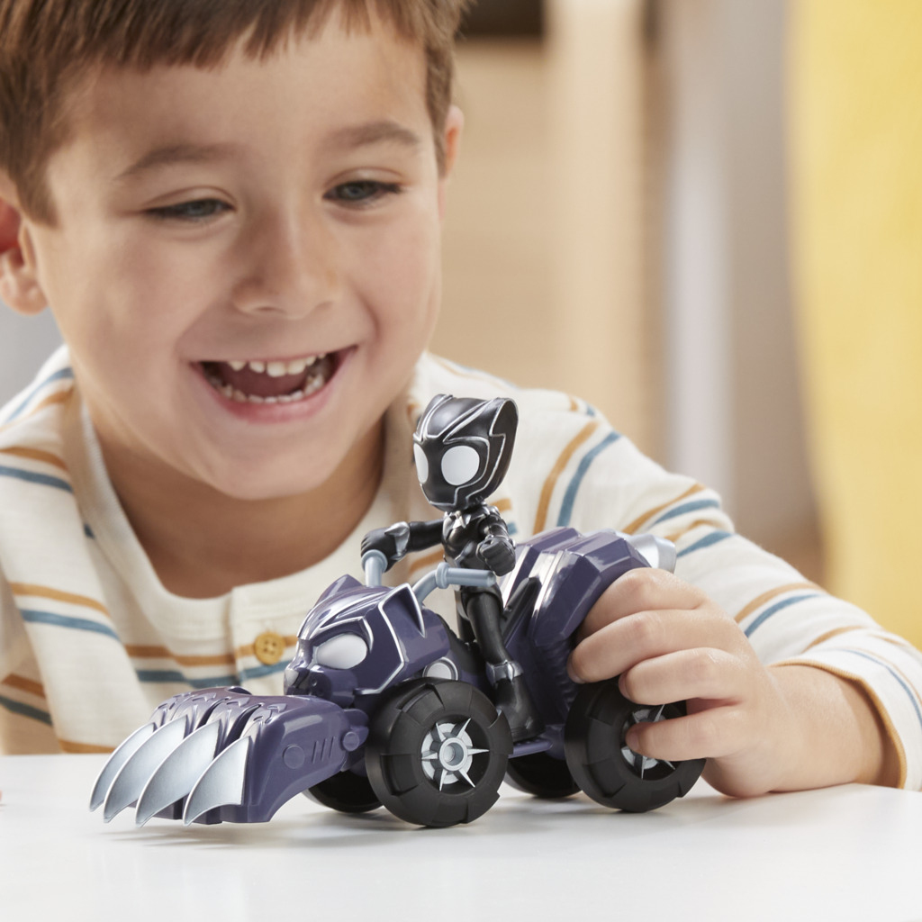 Uśmiechnięty chłopiec trzyma zabawkę Czarnej Pantery na fioletowym quadzie. Zabawka ma srebrne pazury. Chłopiec ma na sobie koszulę w paski.