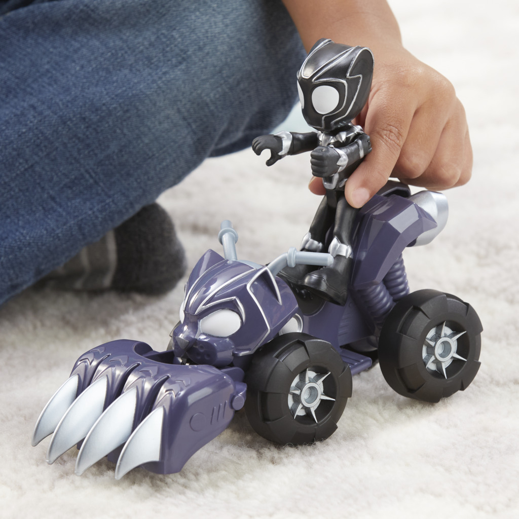 Ręka dziecka trzyma zabawkę Czarnej Pantery na fioletowym ATV. ATV ma kocie cechy i srebrne akcenty. Dżinsy i dywan w tle.