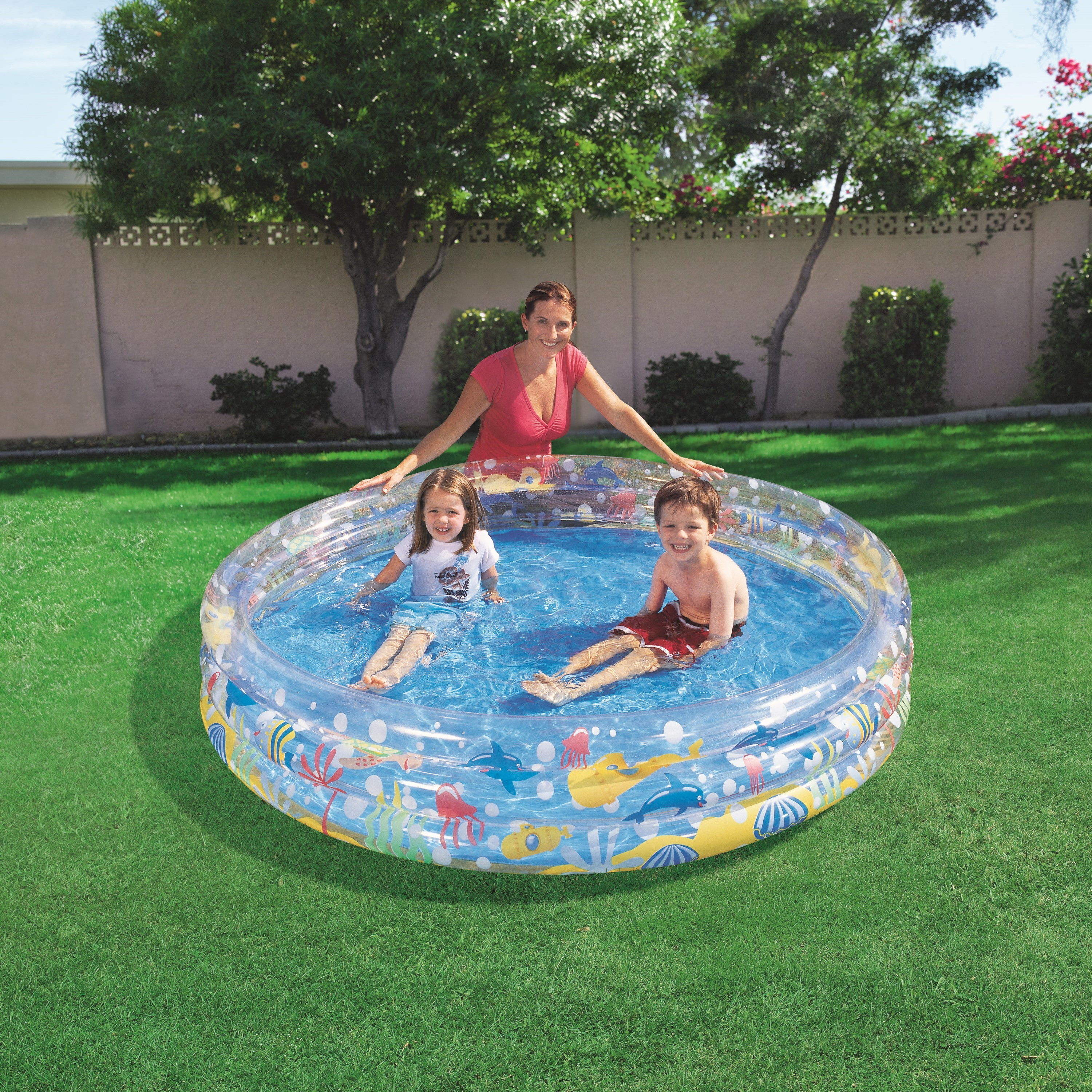 Eine Frau und zwei Kinder in einem Pool. Der Pool befindet sich in einem Garten mit grünem Gras und Bäumen.