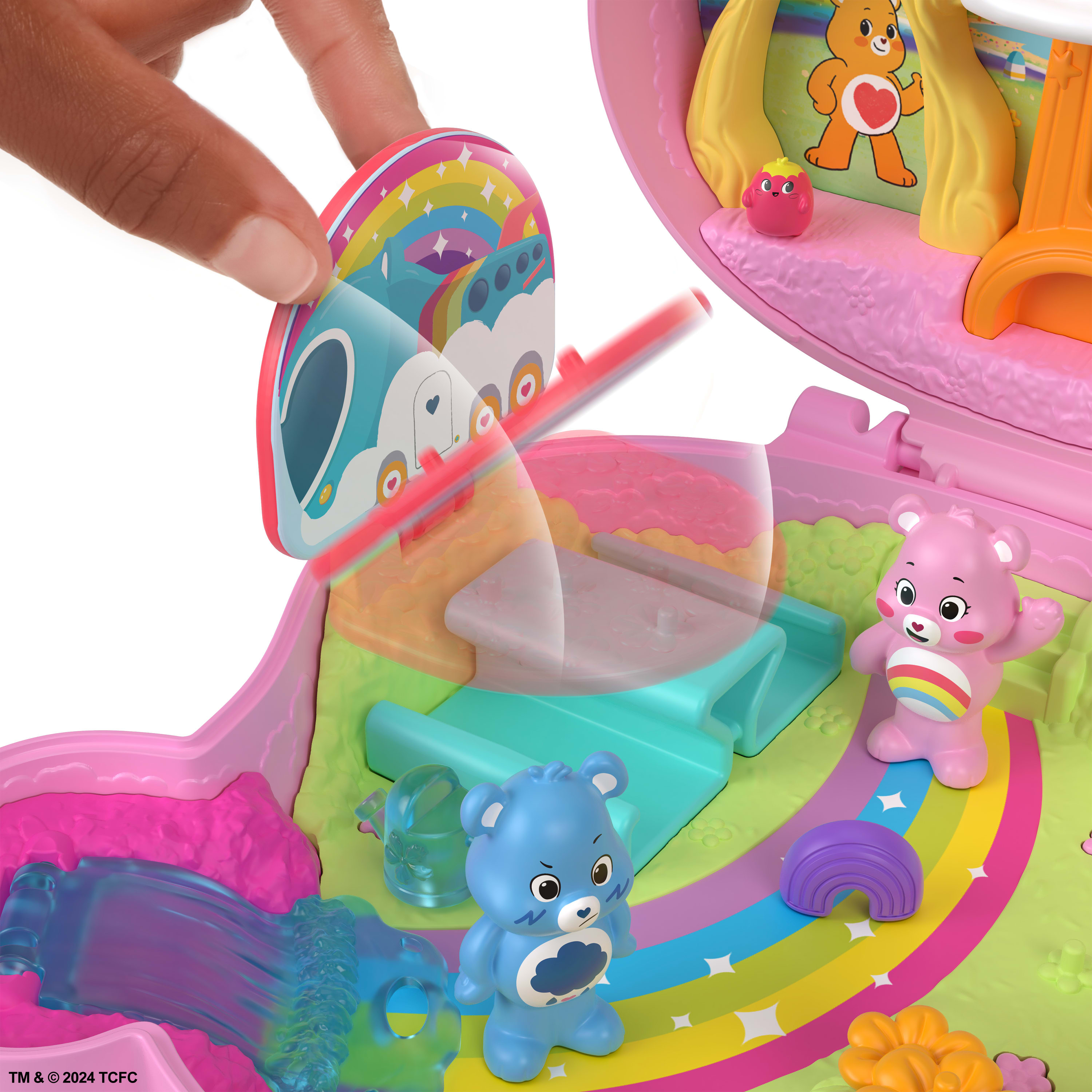 Ręka otwiera zestaw do zabawy Care Bears z misiami, tęczami i samochodem w kształcie chmury. Widoczne są jasne kolory i szczegóły zabawek.