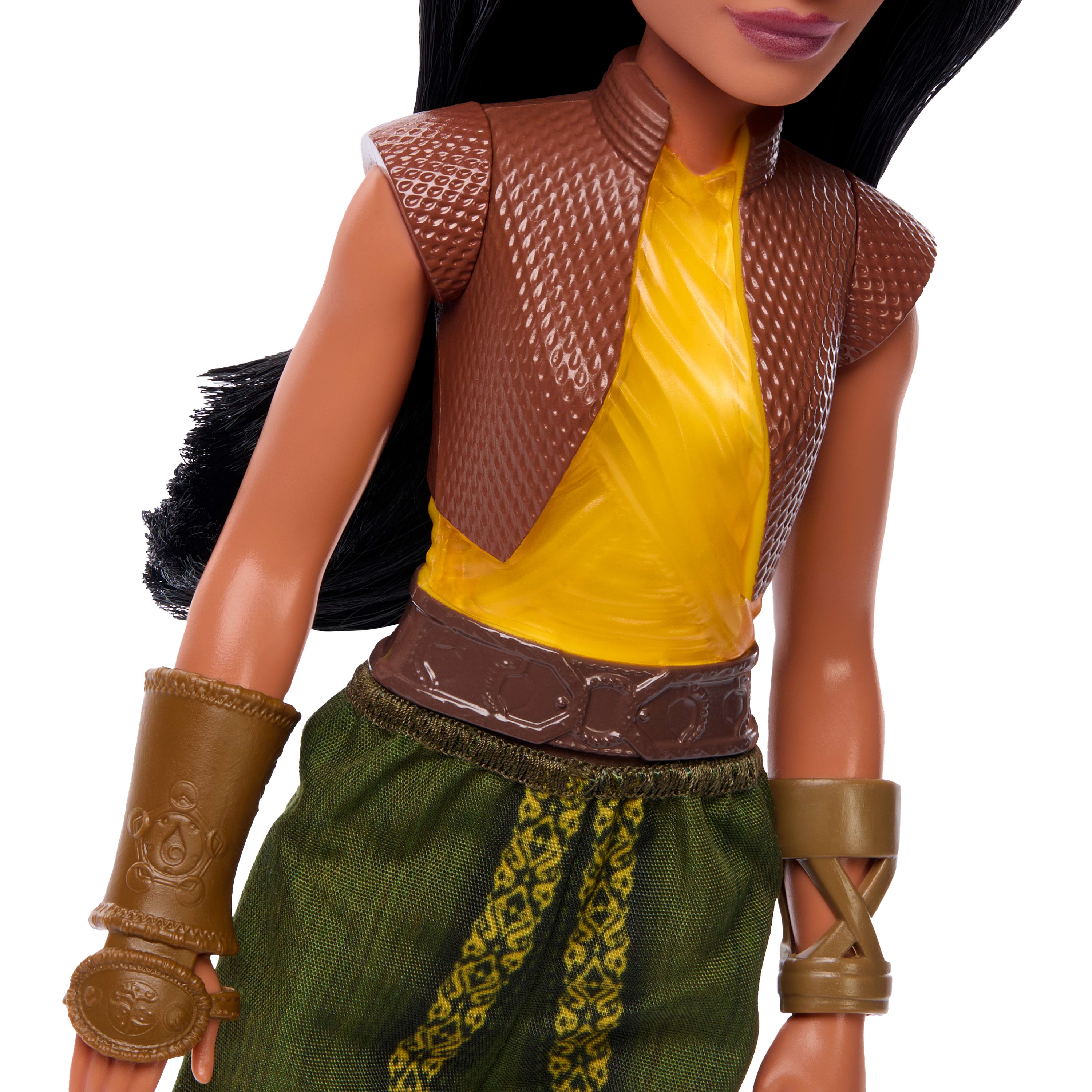 Lalka w brązowej kamizelce na żółtej koszuli, zielonych spodniach i opaskach na ramiona. Czarne włosy i brązowa skóra.