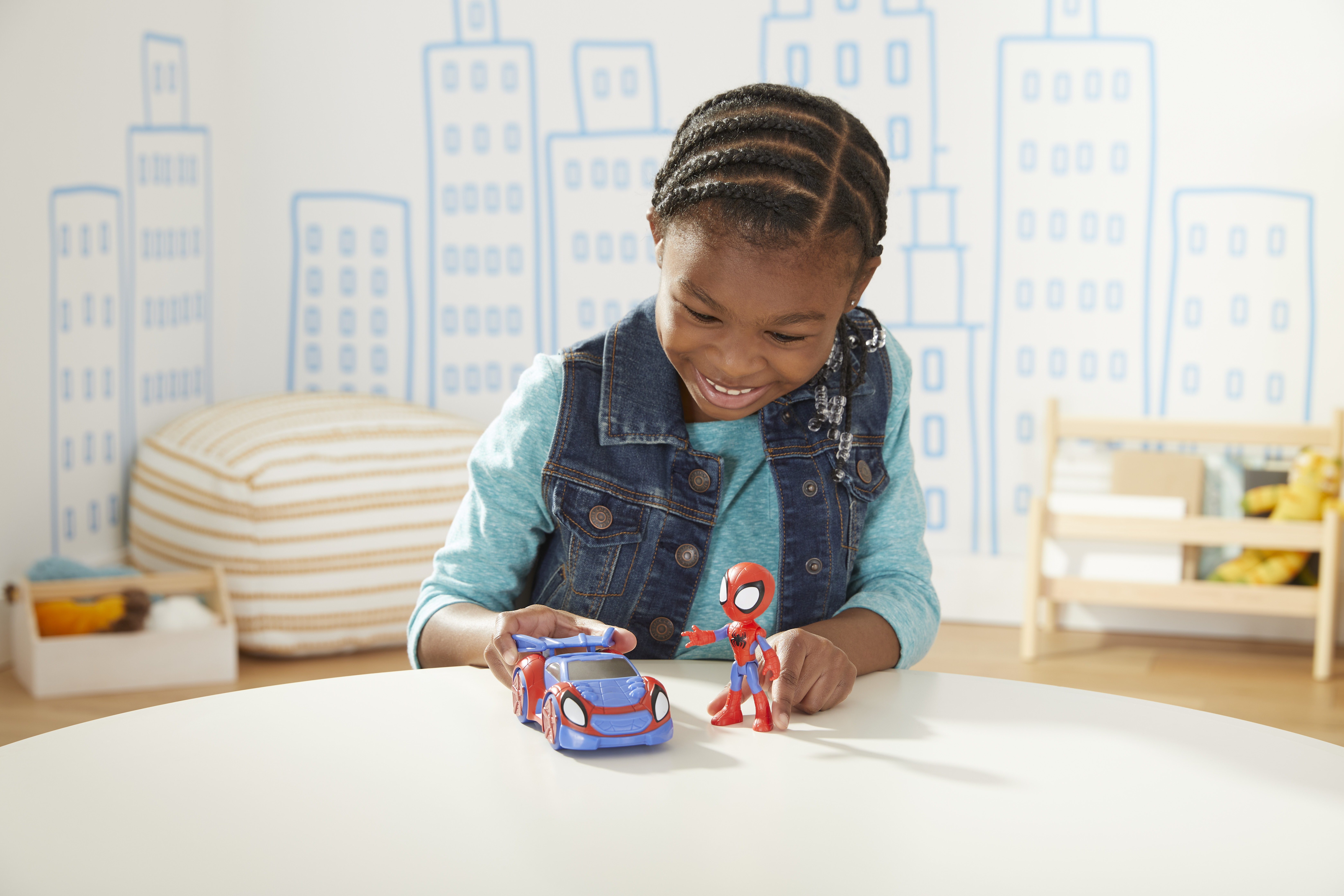 Dziewczyna uśmiecha się do Spidermana i zabawkowego samochodu. Rysunki miast na ścianie.