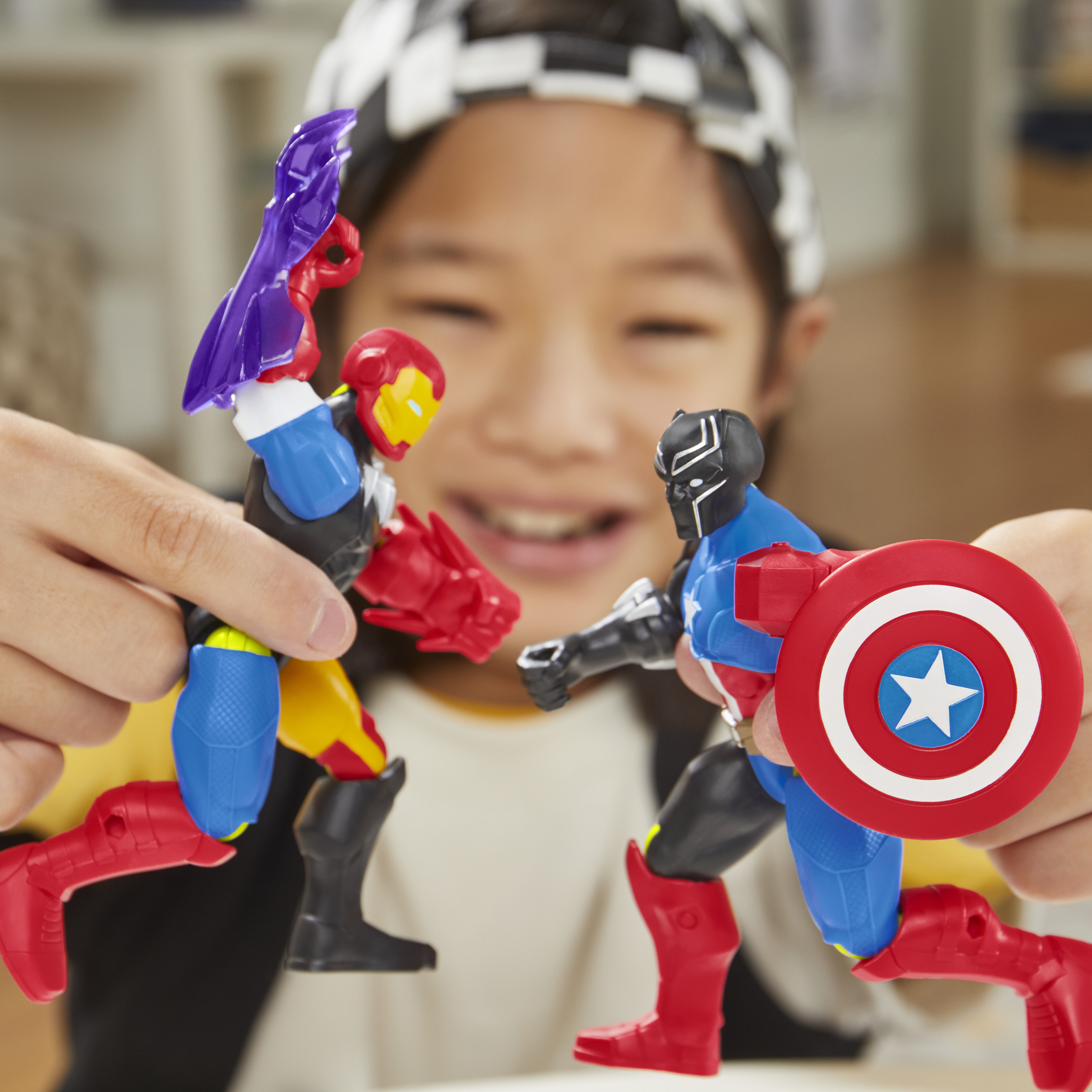 Ein Kind hält Superhelden-Spielzeuge: Iron Man und Captain America. Die Spielzeuge befinden sich in einer Kampfpose, wobei das Kind im Hintergrund lächelt.