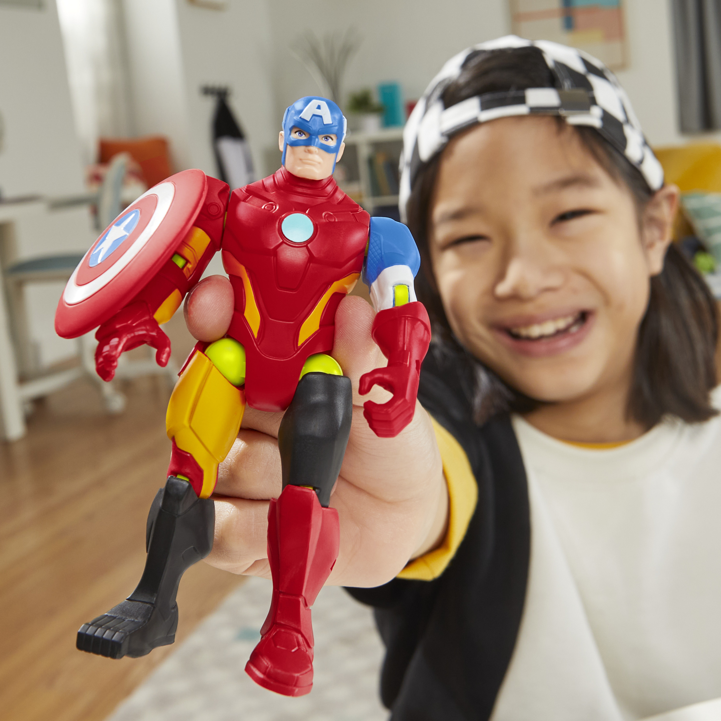 Ein Kind hält ein Spielzeug. Es ist eine Captain America und Iron Man Hybridfigur. Das Kind lächelt vor einem häuslichen Hintergrund.