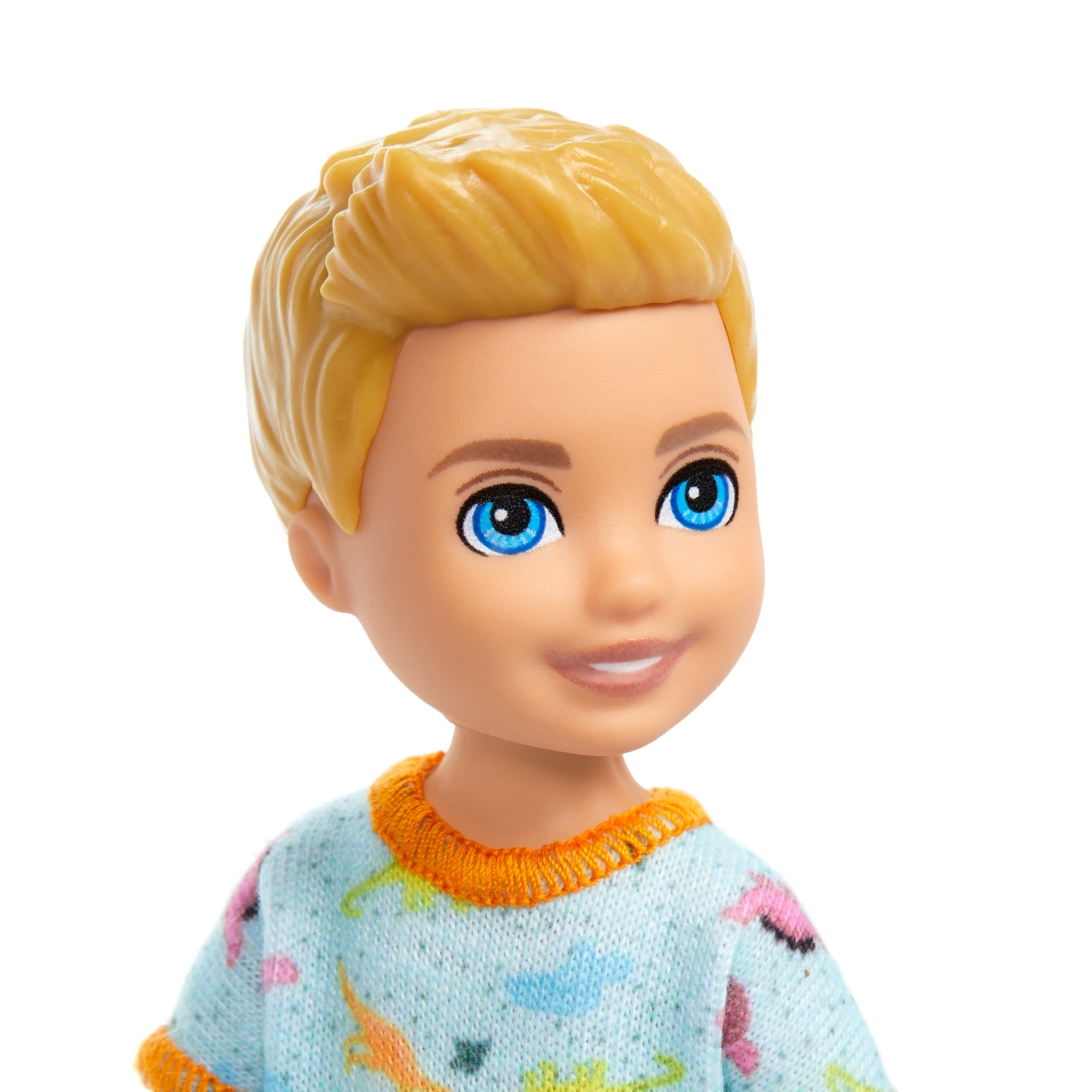 Ein Puppenkopf mit blonden Haaren und blauen Augen. Sie trägt einen hellblauen Pullover mit orangefarbenem Besatz und Dinosaurierdrucken.
