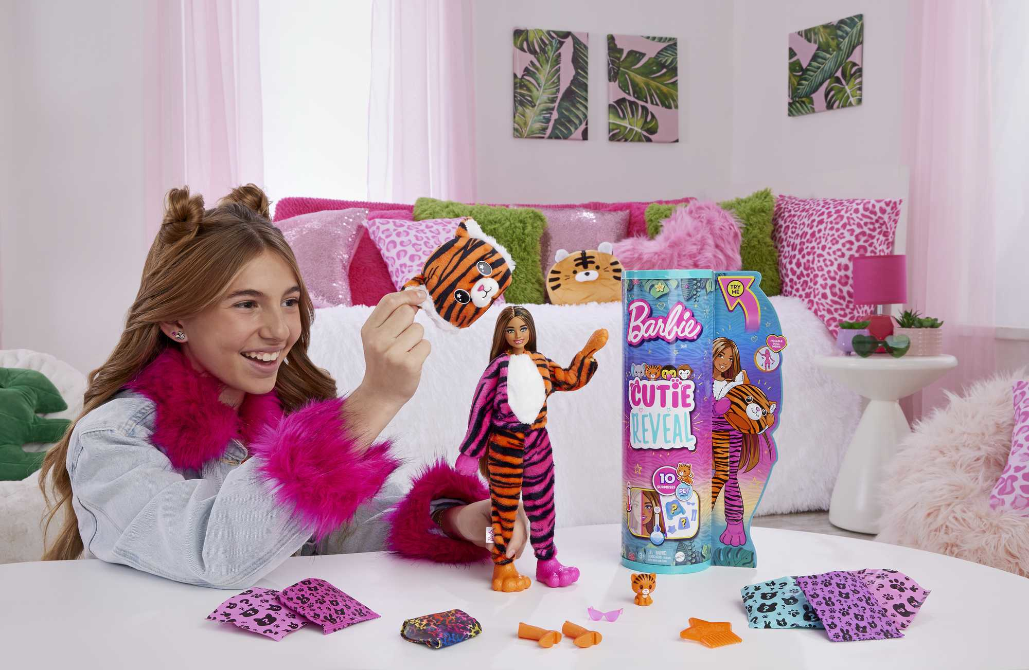 Ein Mädchen hält ein Tiger-Spielzeug. Eine Barbie-Puppe als Tiger steht auf einem Tisch. Tigerkissen und Dekorationen sind im Hintergrund.