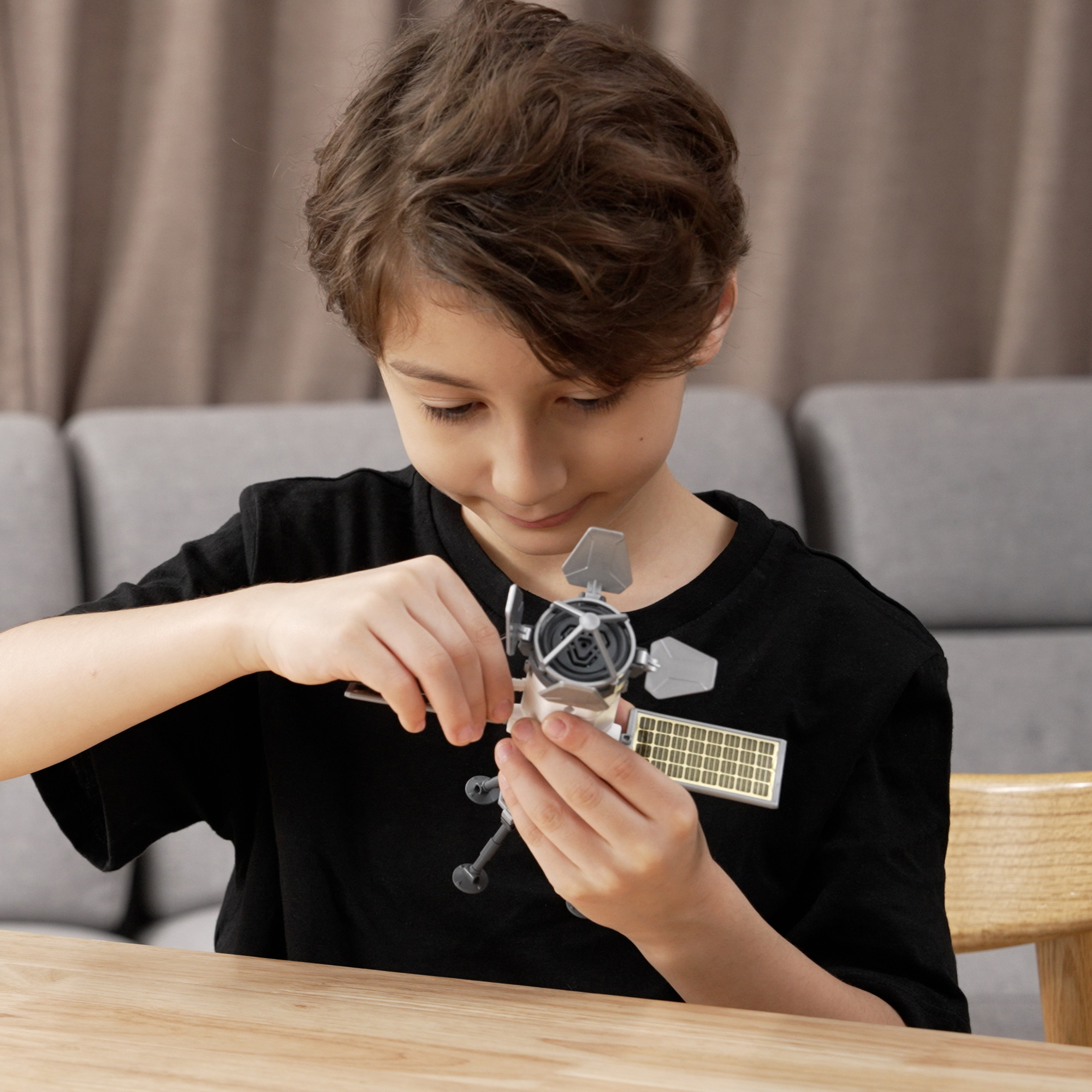 Chłopiec w czarnej koszulce montuje model satelity na drewnianym stole.