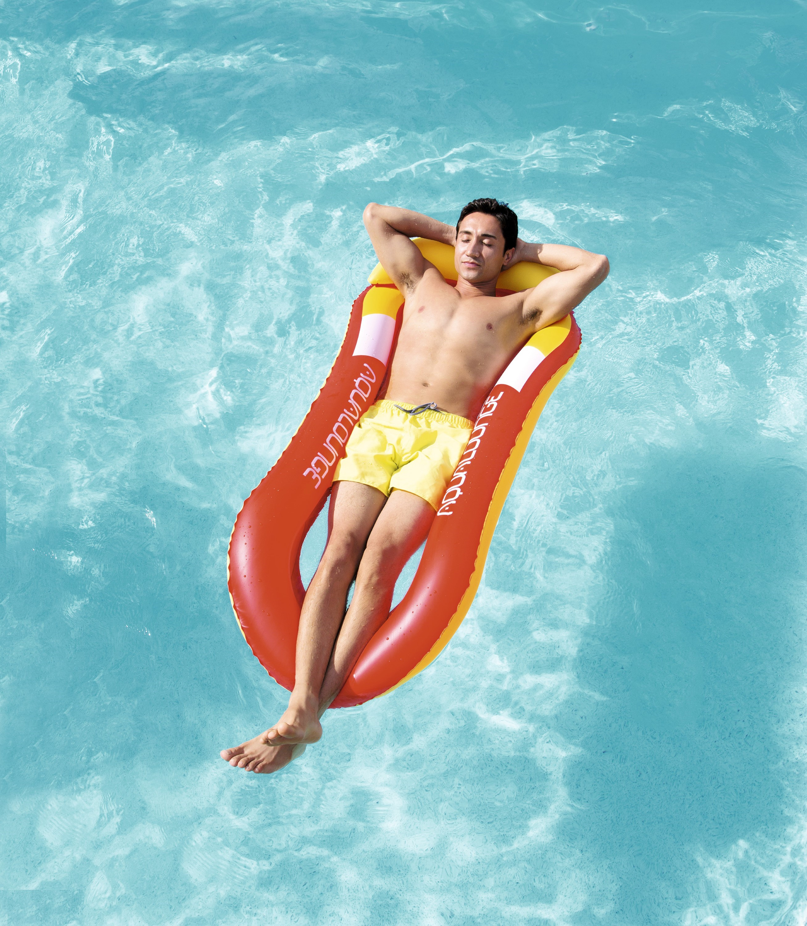 Man ontspant op een rood-gele zwembadfloat in helder blauw water, armen achter het hoofd, ogen gesloten.
