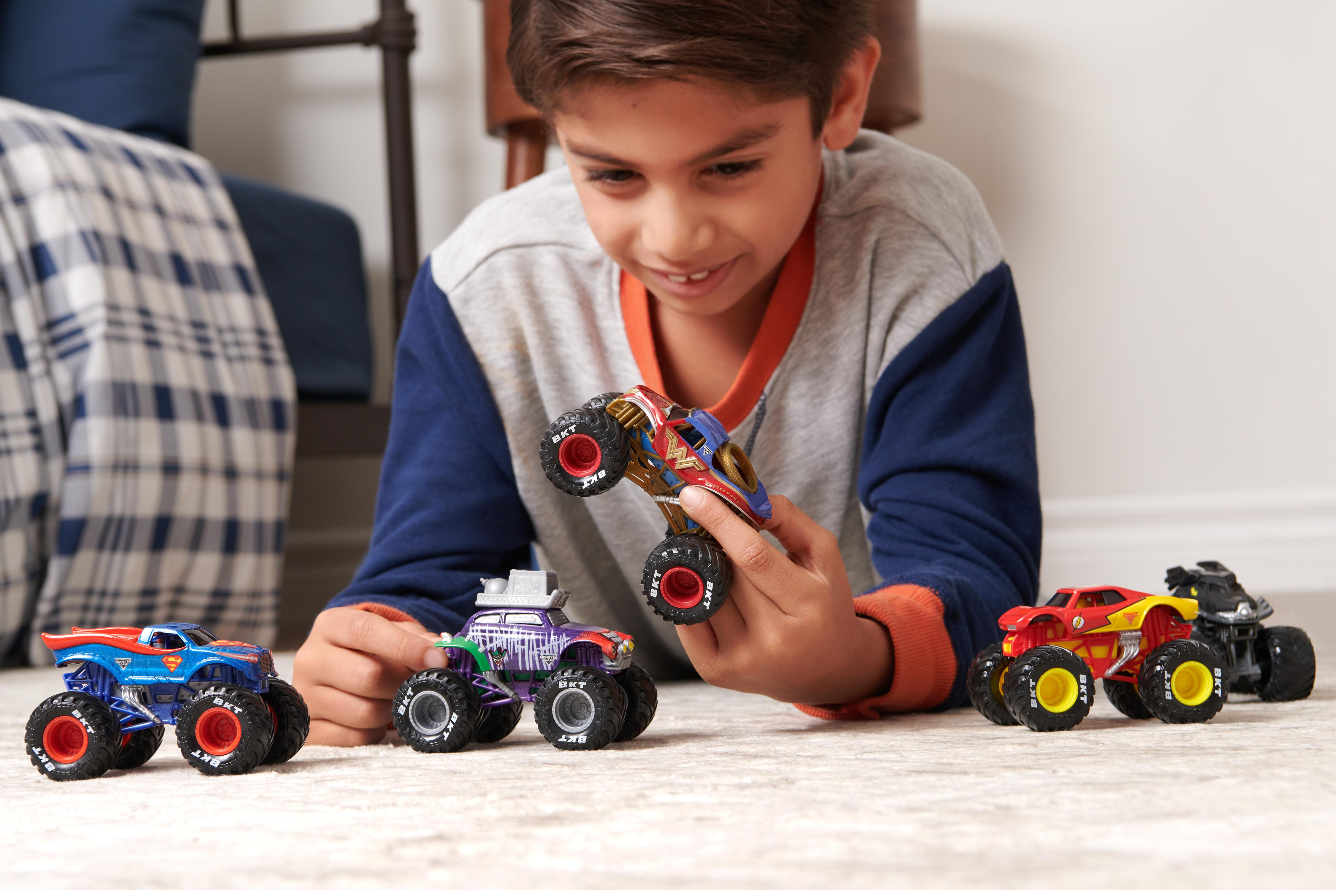 Ein Junge lächelt und hält einen Monstertruck. Andere Trucks liegen auf dem Boden. Im Hintergrund sind ein Bett und eine Wand.