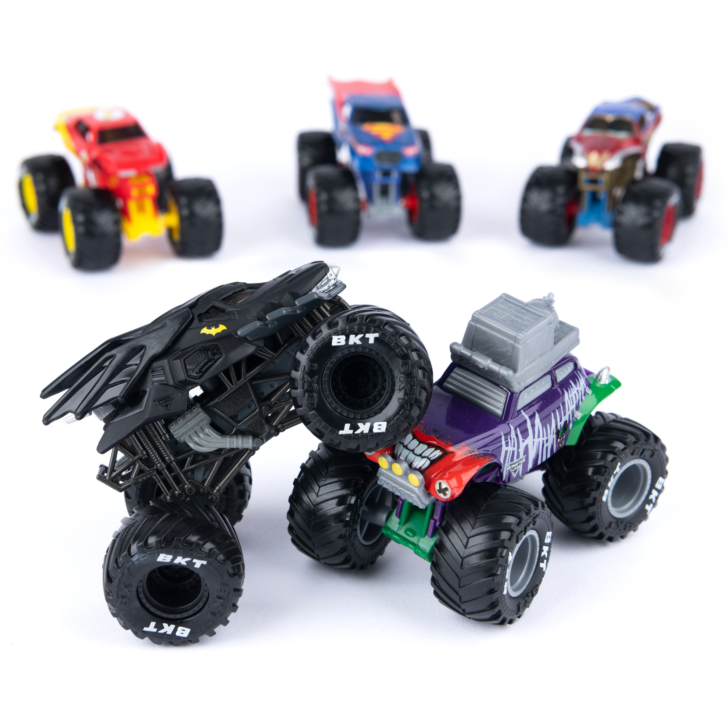 Monster Jam Trucks: Batman und Joker im Fokus, Superman und andere verschwommen im Hintergrund auf Weiß.