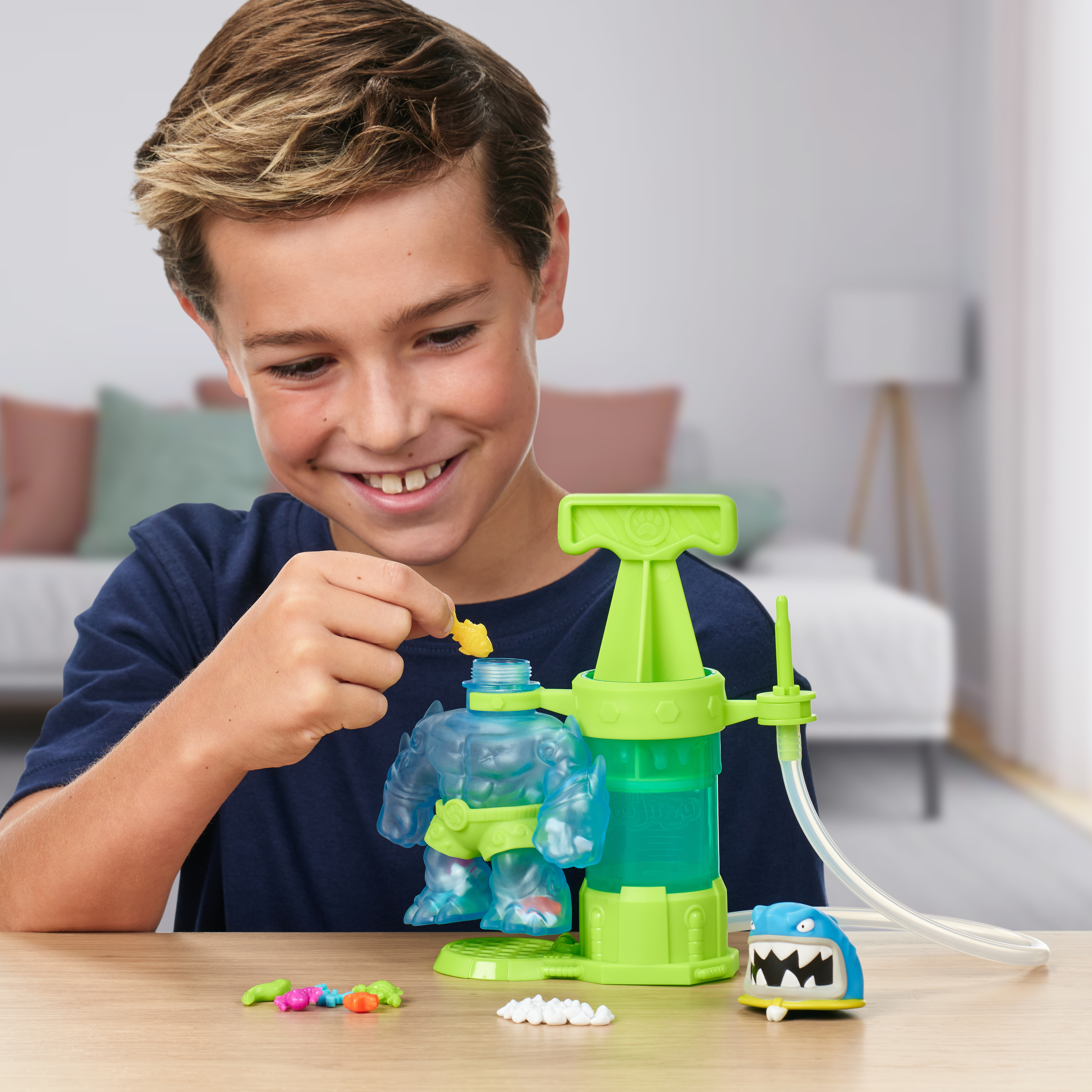 Ein Junge lächelt und fügt einem Spielzeug einen gelben Fisch hinzu. Das Spielzeug ist ein grünes und durchsichtiges Monster-Set.