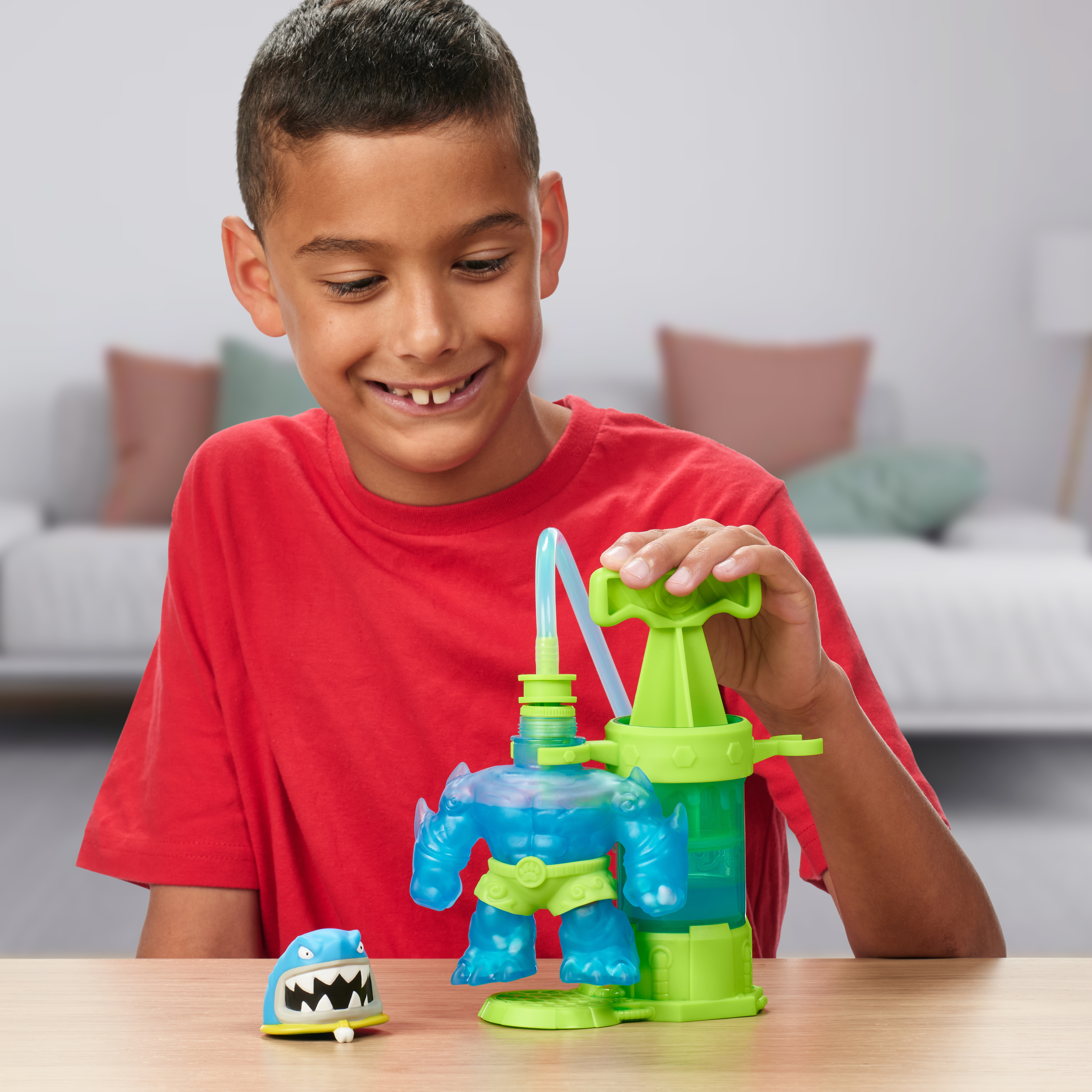 Ein Junge lächelt und spielt mit einem Spielzeugmonster. Das Spielzeug ist blau und grün. Der Hintergrund ist unscharf.