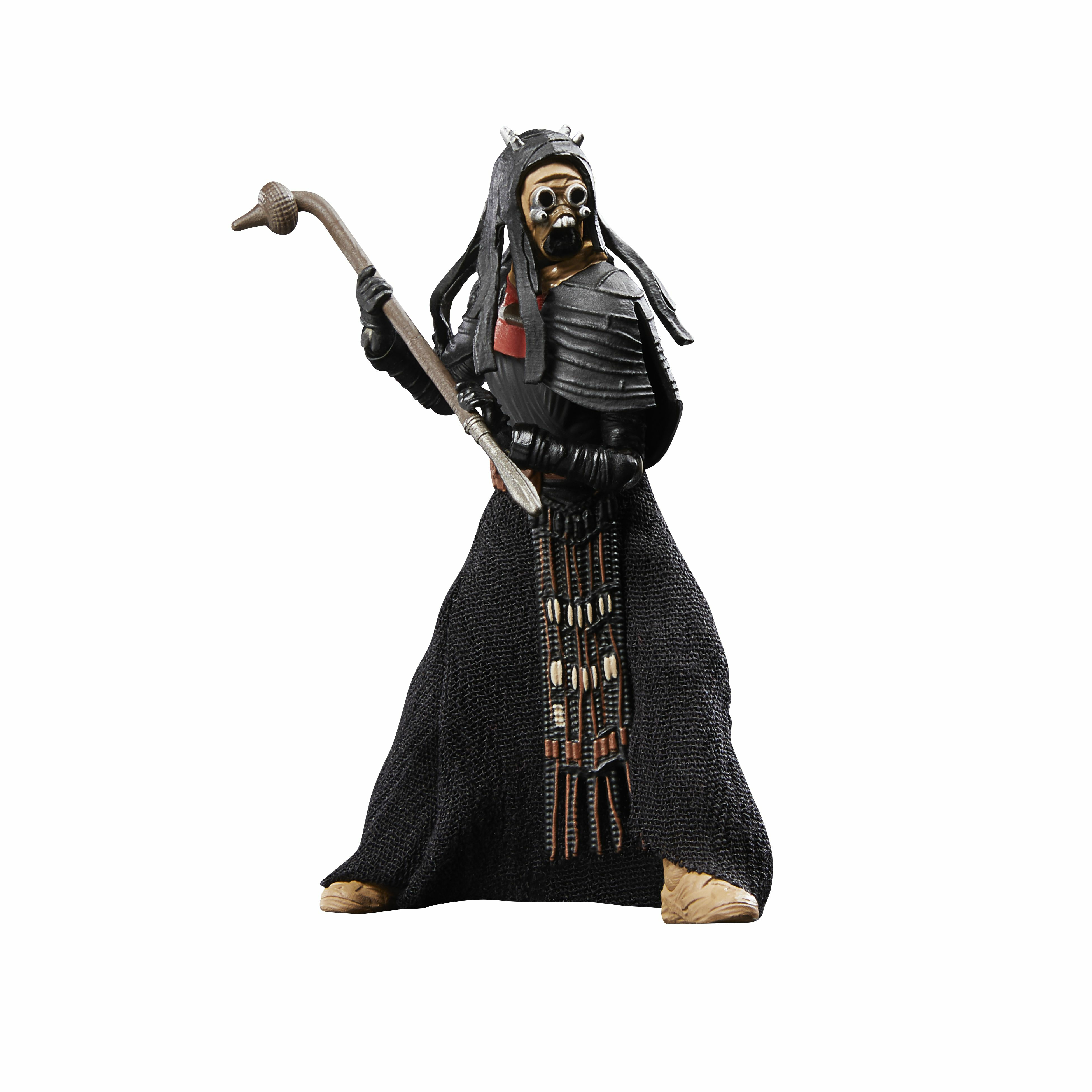 Figura con capa, máscara y capucha negras, sosteniendo un bastón. La figura está sobre fondo blanco.