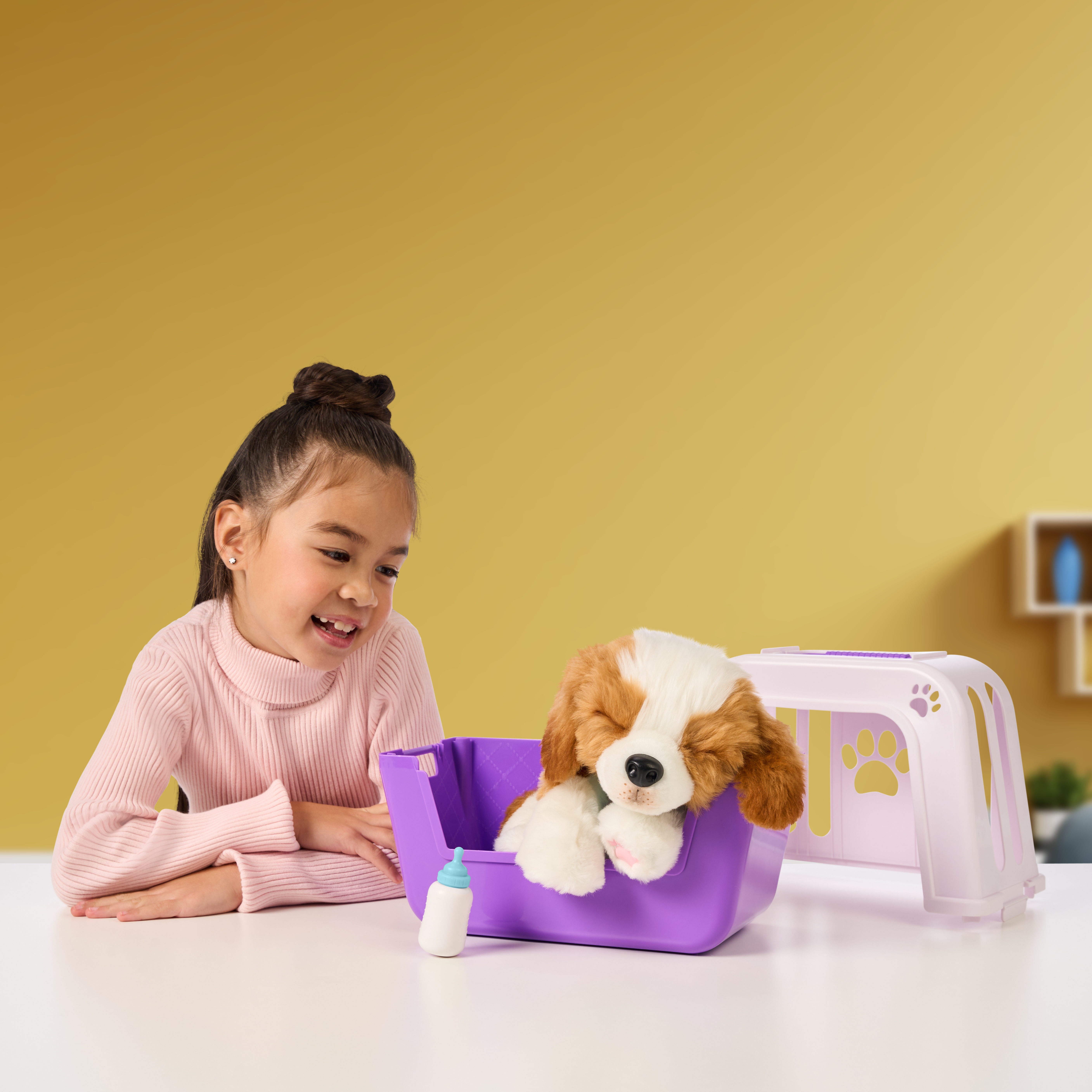 Dziewczynka uśmiecha się do zabawkowego psa w fioletowej transporterze. Butelka stoi obok. Tło jest żółte.