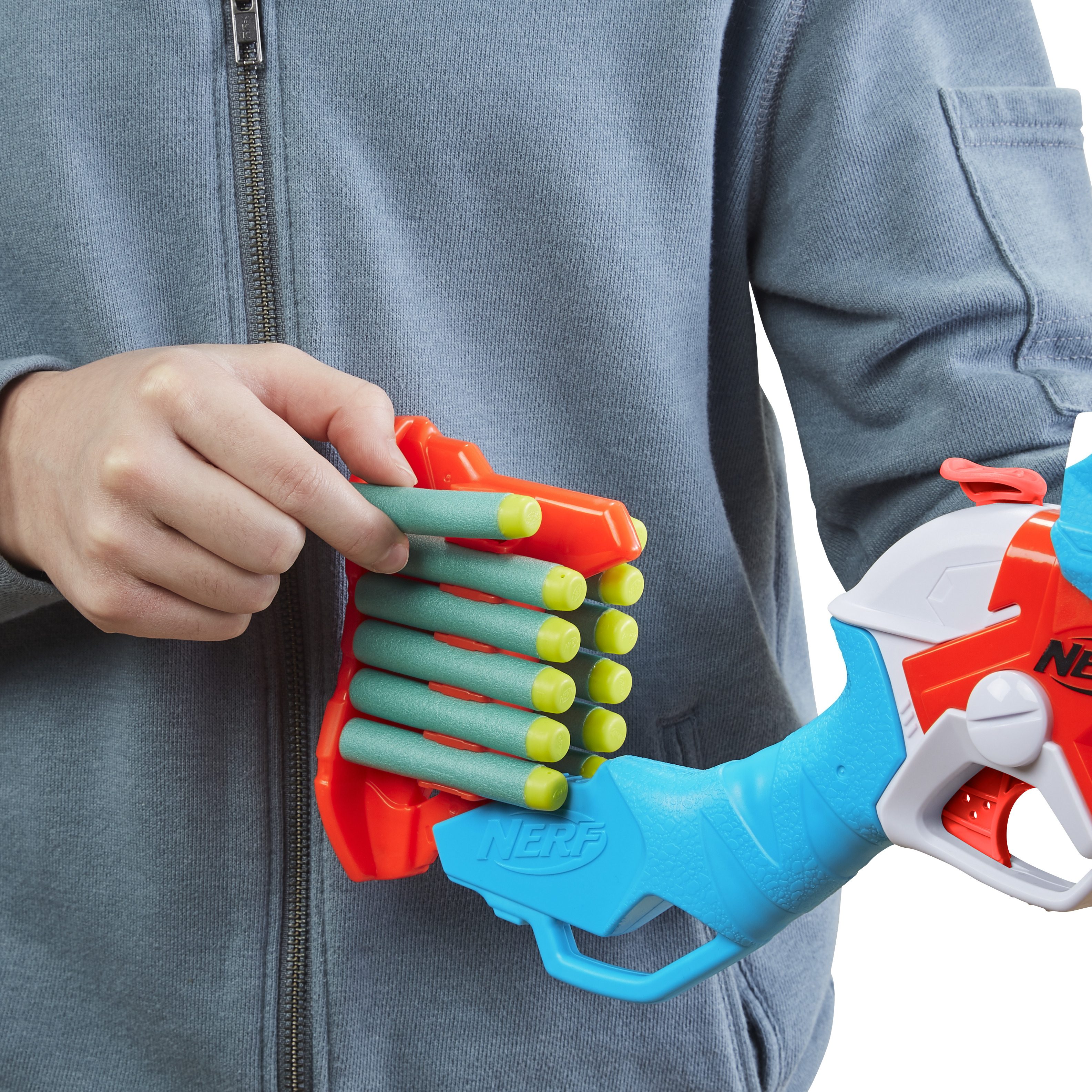 Eine Person hält eine Nerf-Pistole. Die Pistole ist orange, blau und weiß mit grünen Kugeln. Die Person trägt eine graue Jacke.