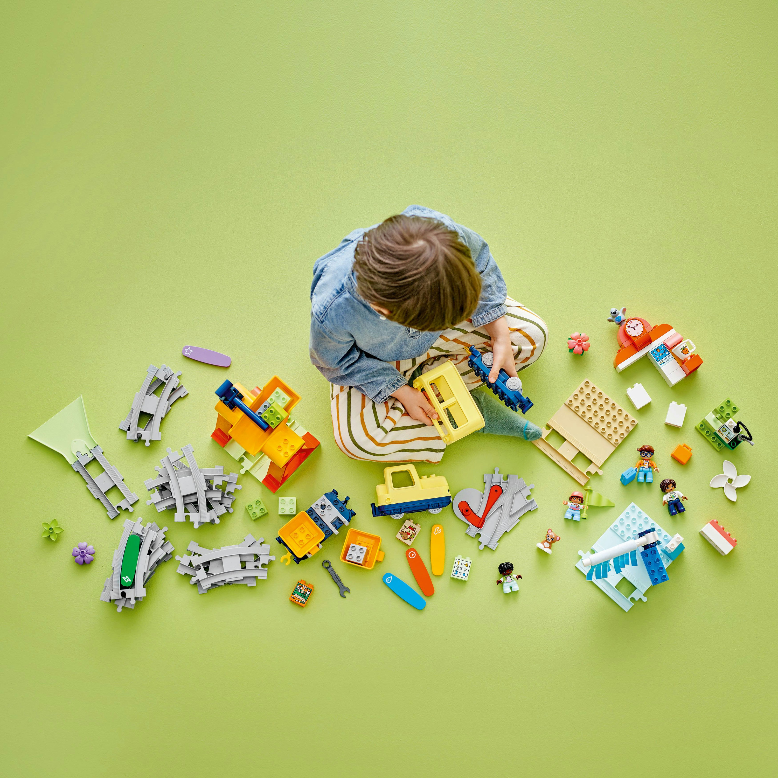 Dziecko bawi się kolorowymi torami kolejowymi i klockami na zielonej powierzchni.