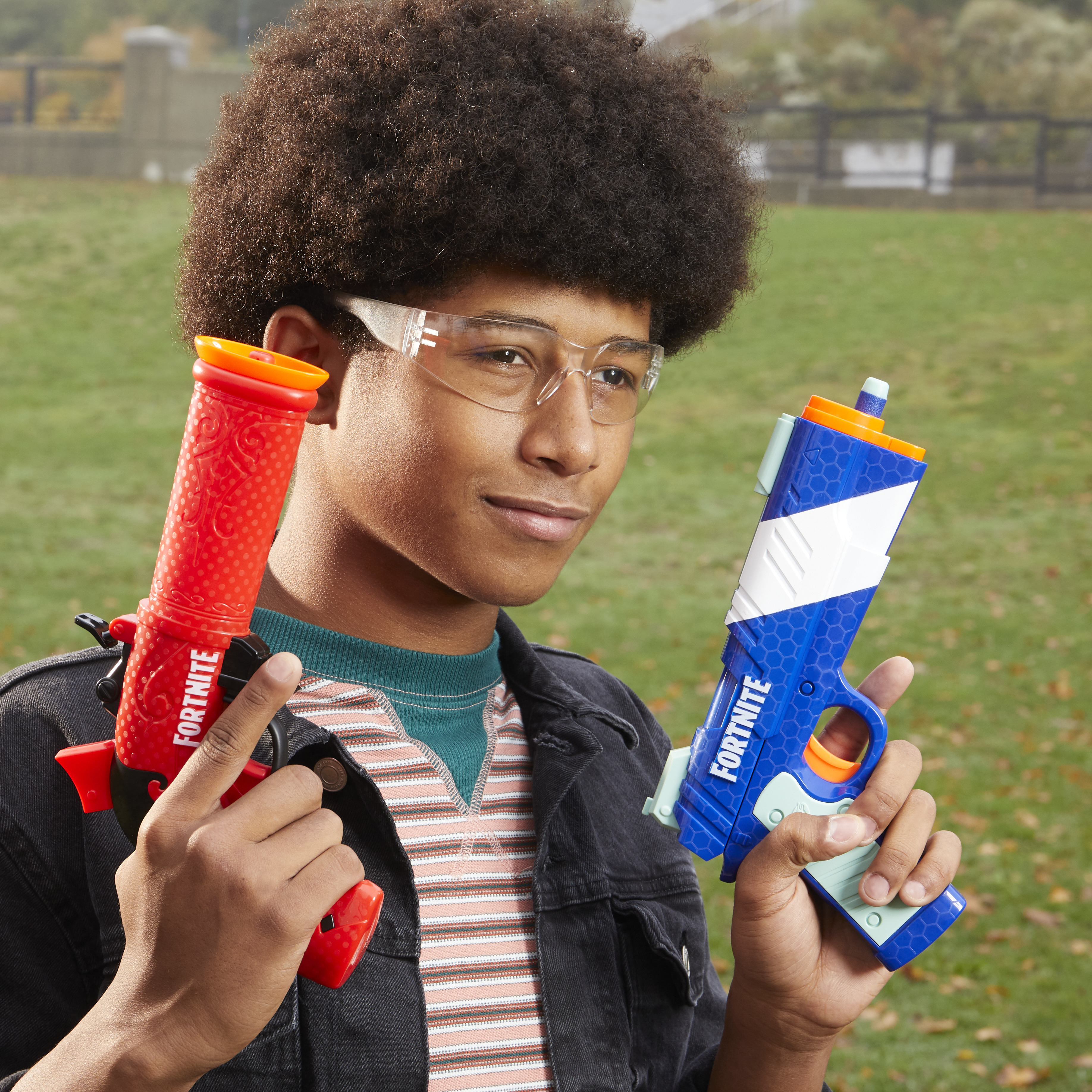Nastolatek trzyma dwa pistolety zabawki. Jeden czerwony, drugi niebieski. Ma okulary i czarną kurtkę, z zieloną i pasiastą koszulą.