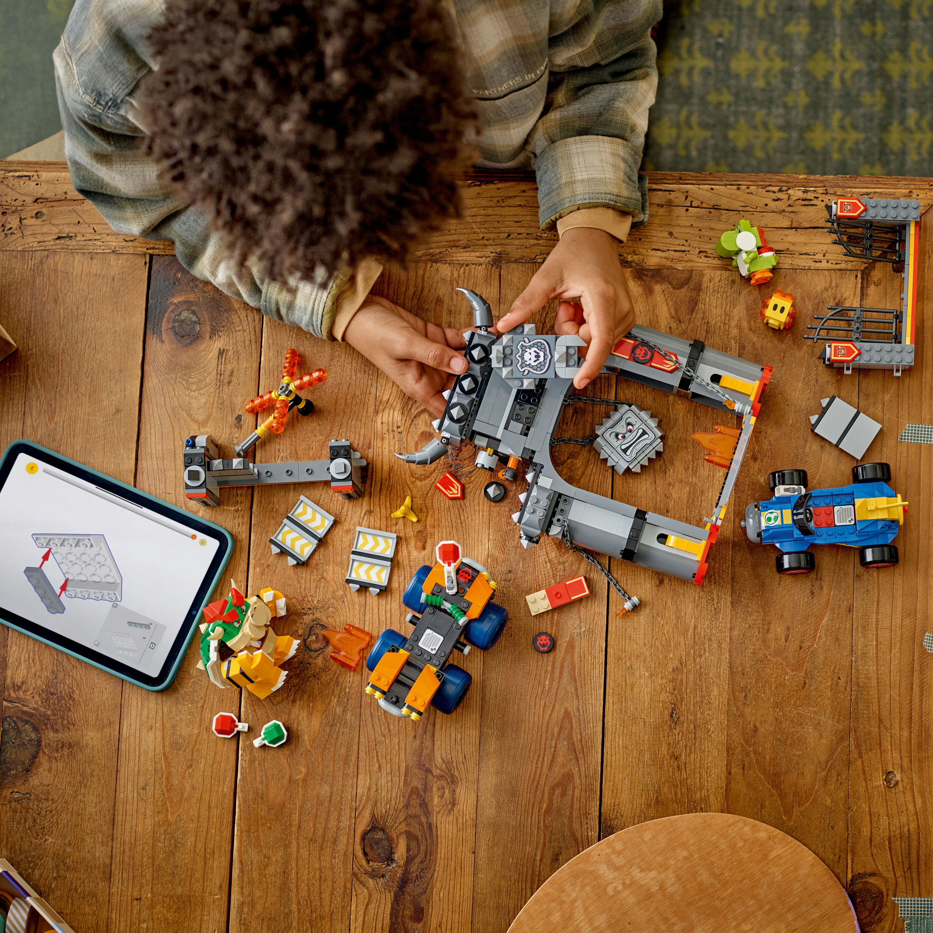 Ahşap bir masada Lego seti yapan bir kişi. Set, Mario evreninden arabalar ve karakterler içerir.