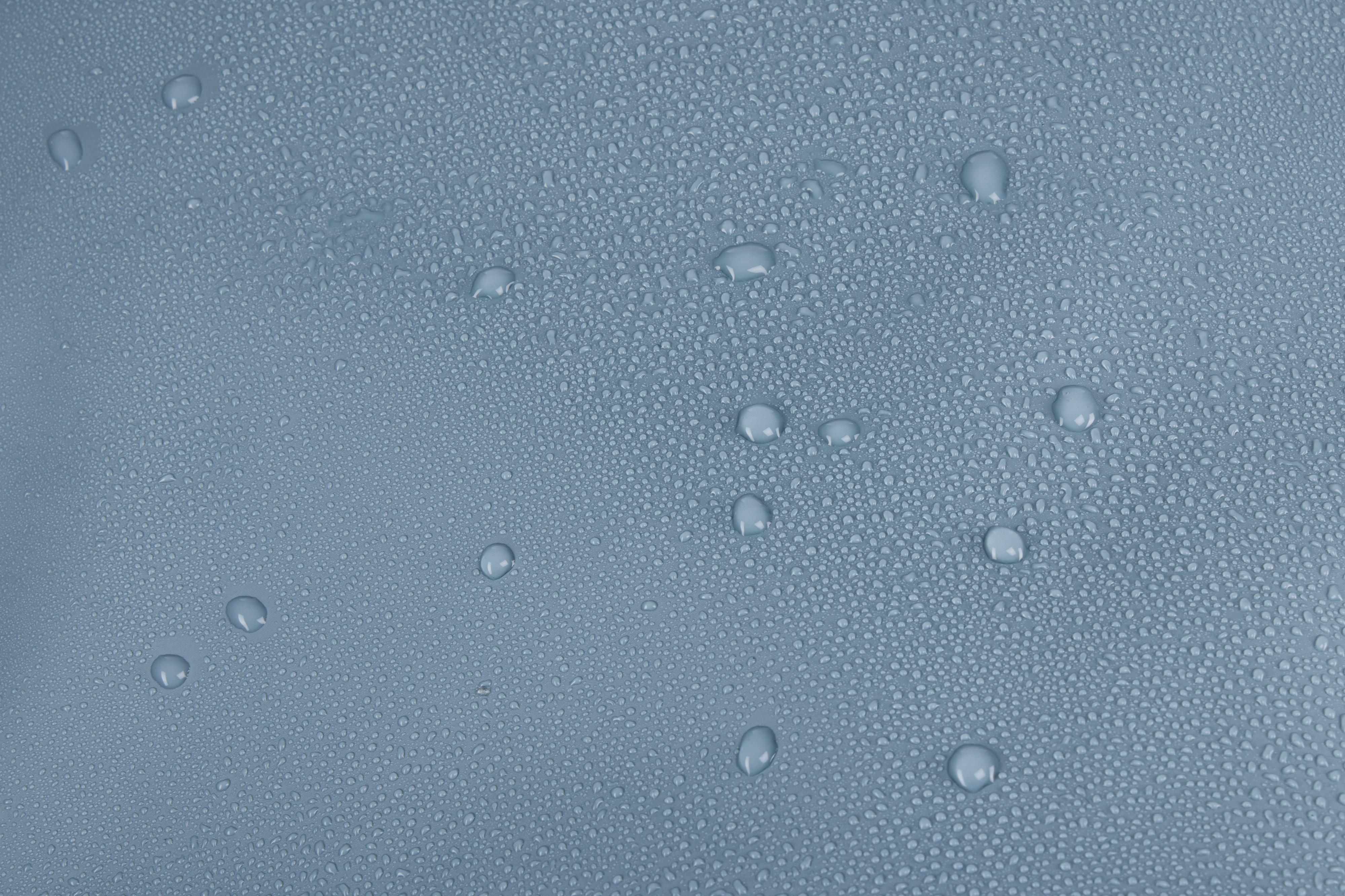 Zbliżenie niebieskiej powierzchni pokrytej małymi i dużymi kroplami wody.