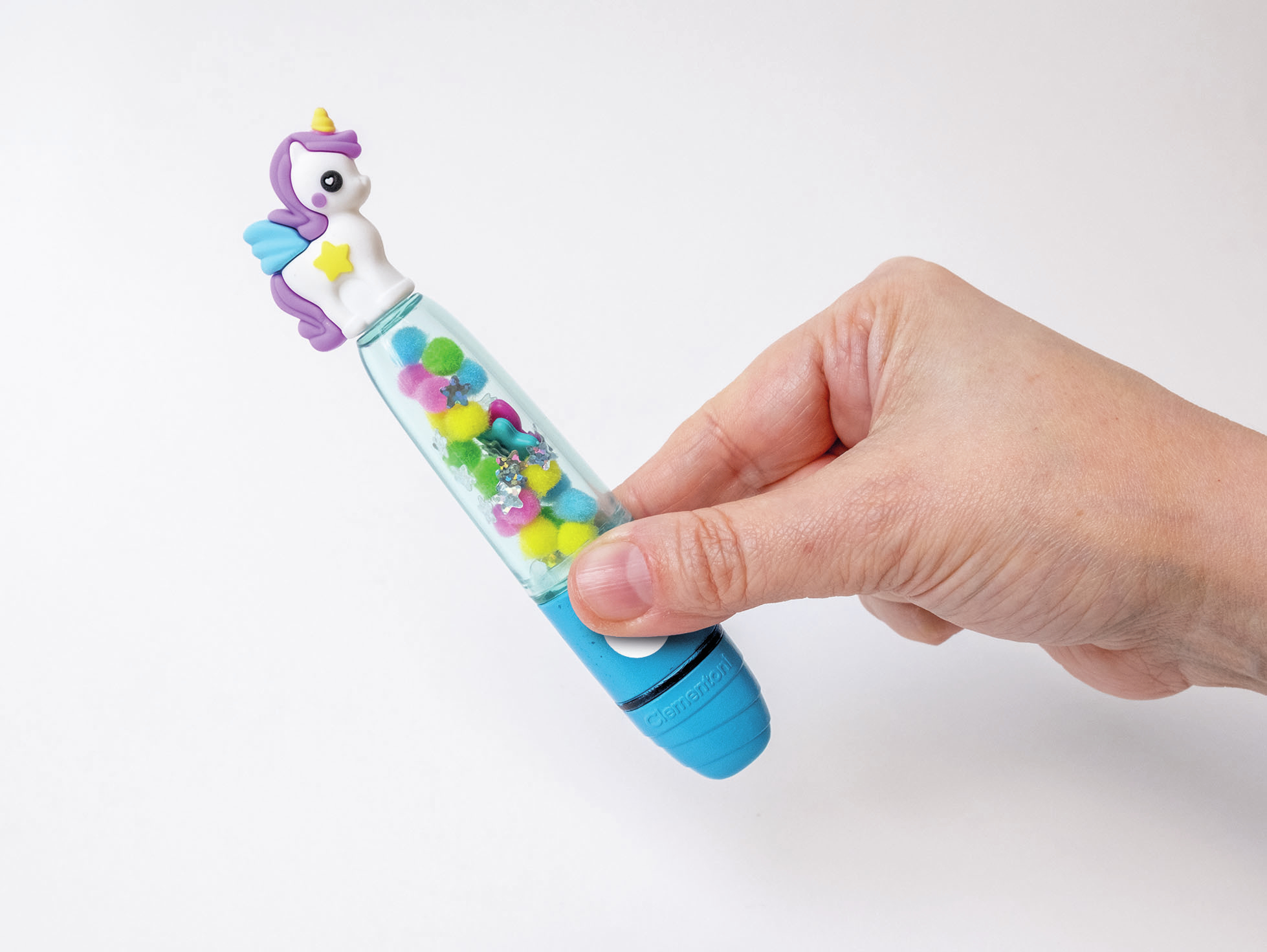Ręka trzyma niebieski długopis ozdobiony jednorożcem, w środku kolorowe pompony i brokat.