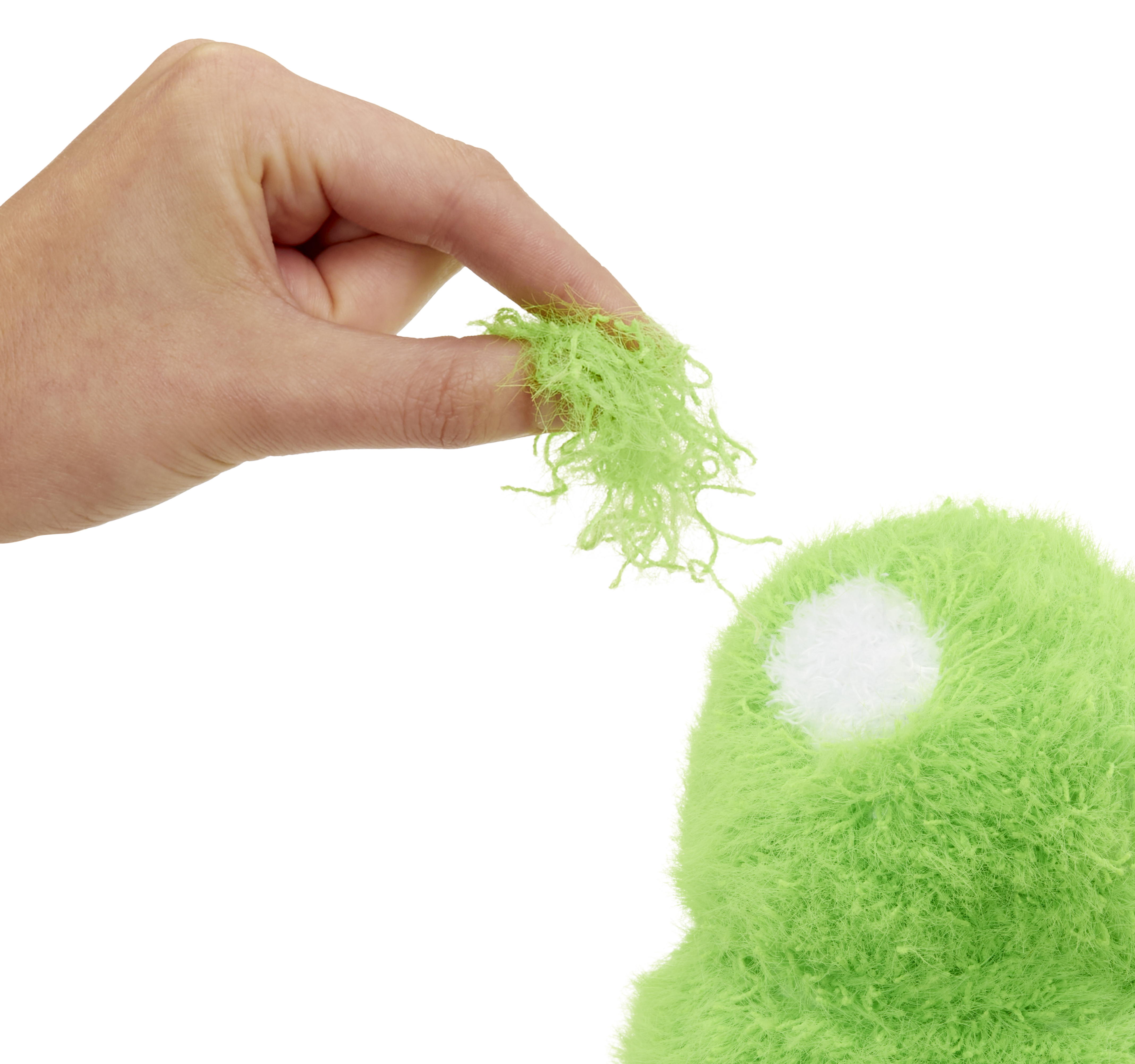 Ręka trzyma zielony, puszysty materiał nad zielonym obiektem z białą plamą. Białe tło.