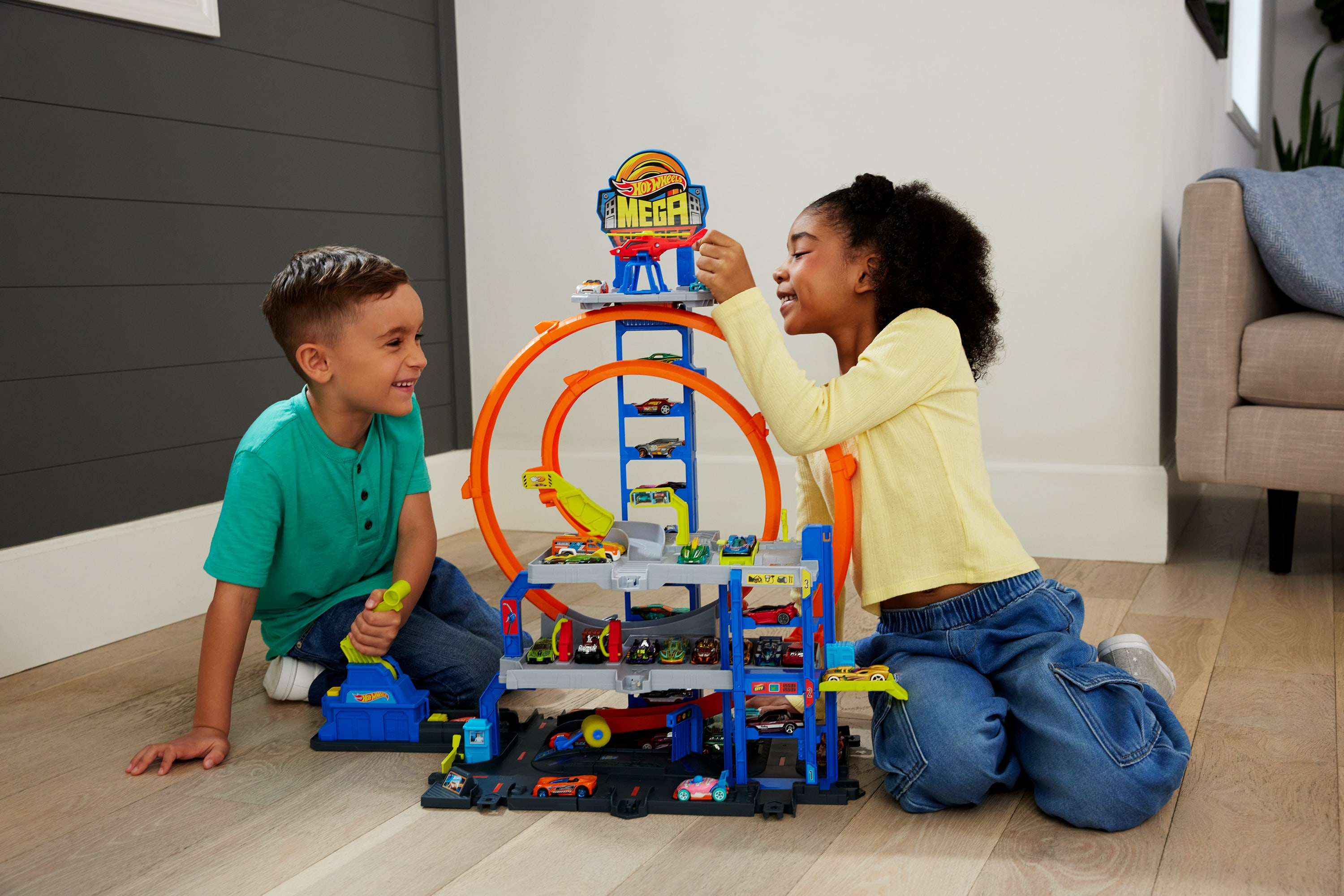 Dwoje dzieci bawi się garażem z zabawkami Hot Wheels. Chłopiec trzyma dźwignię, a dziewczynka wskazuje na garaż.