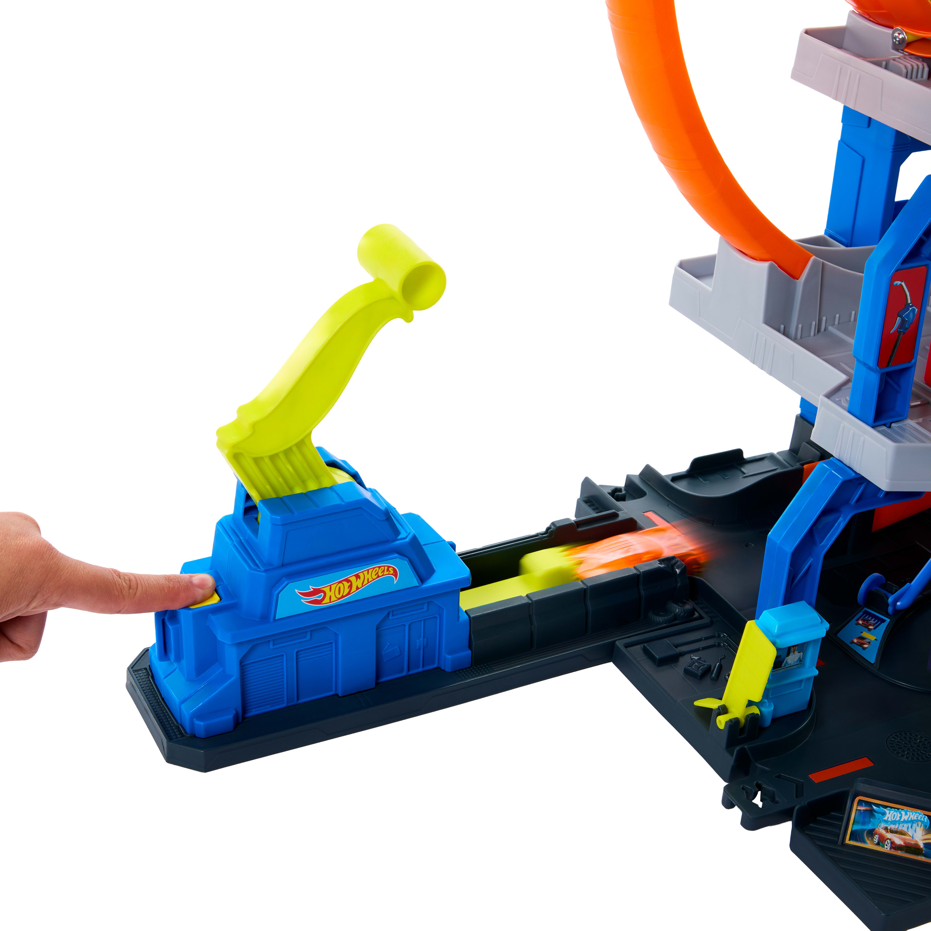 Ręka naciska żółty przycisk na niebieskiej zabawce Hot Wheels. Pomarańczowa pętla jest po prawej.