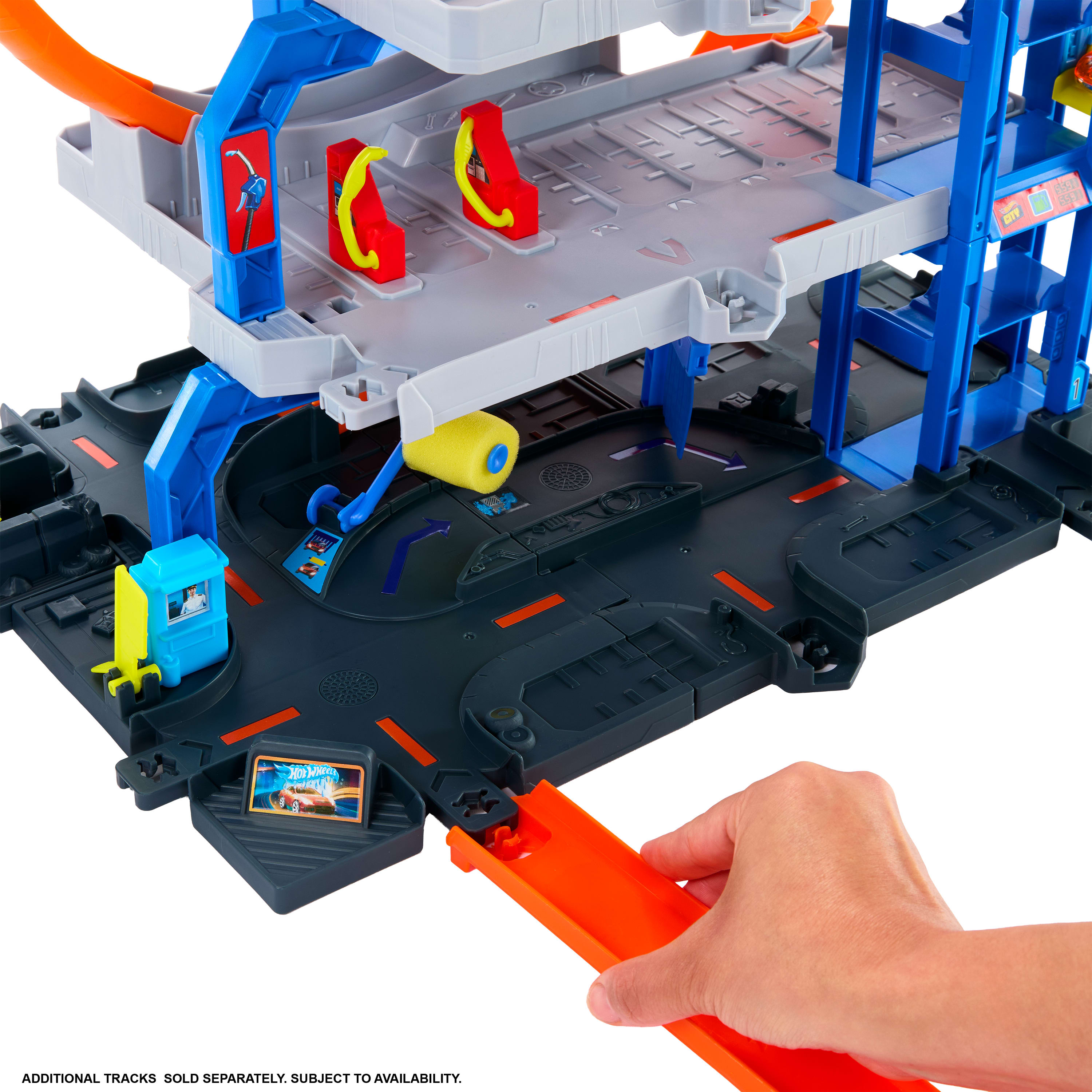 Zestaw do zabawy Hot Wheels. Zawiera wiele poziomów, dystrybutory paliwa i dłoń trzymającą pomarańczowy element toru.