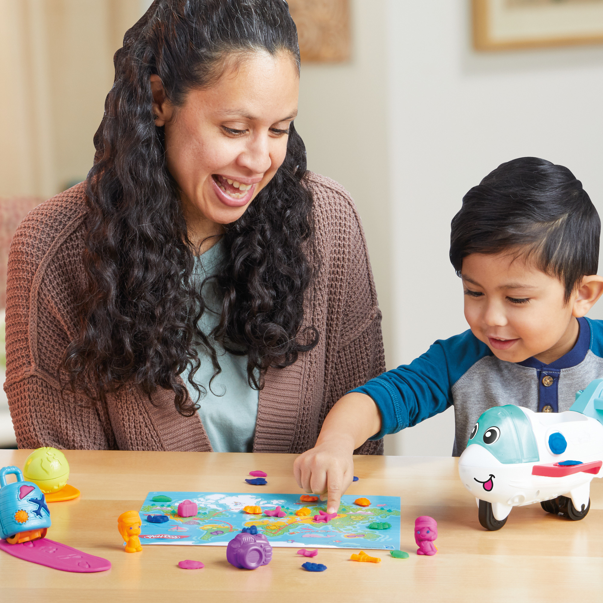 Una mujer y un niño jugando con un juego de mapa mundial. El niño señala el mapa, un avión de juguete está a su lado.