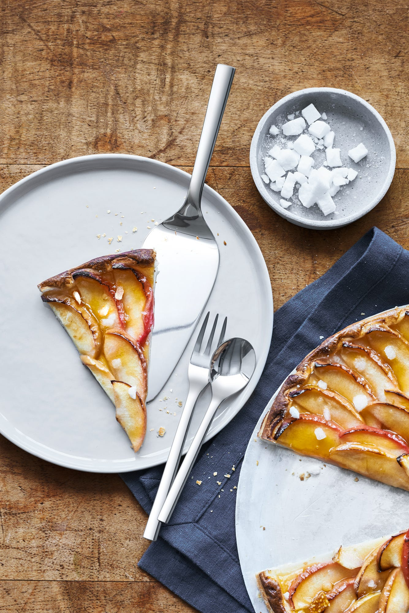 Vue aérienne de tartes aux pommes sur des assiettes avec des ustensiles. Table en bois, morceaux de glace dans un petit bol et une serviette bleue.